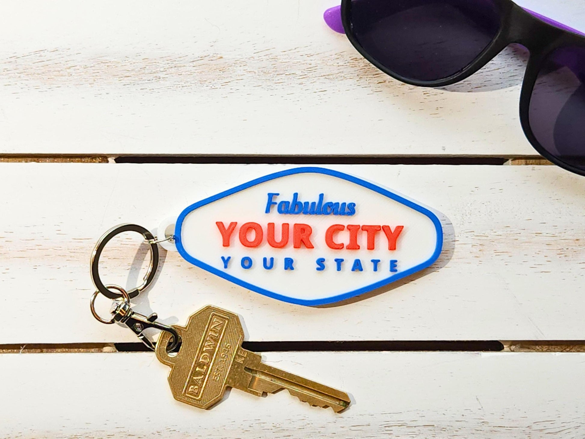 Personalized Fabulous city keychain with YOUR CITY / YOUR STATE design styled with keys and sunglasses on white wood surface