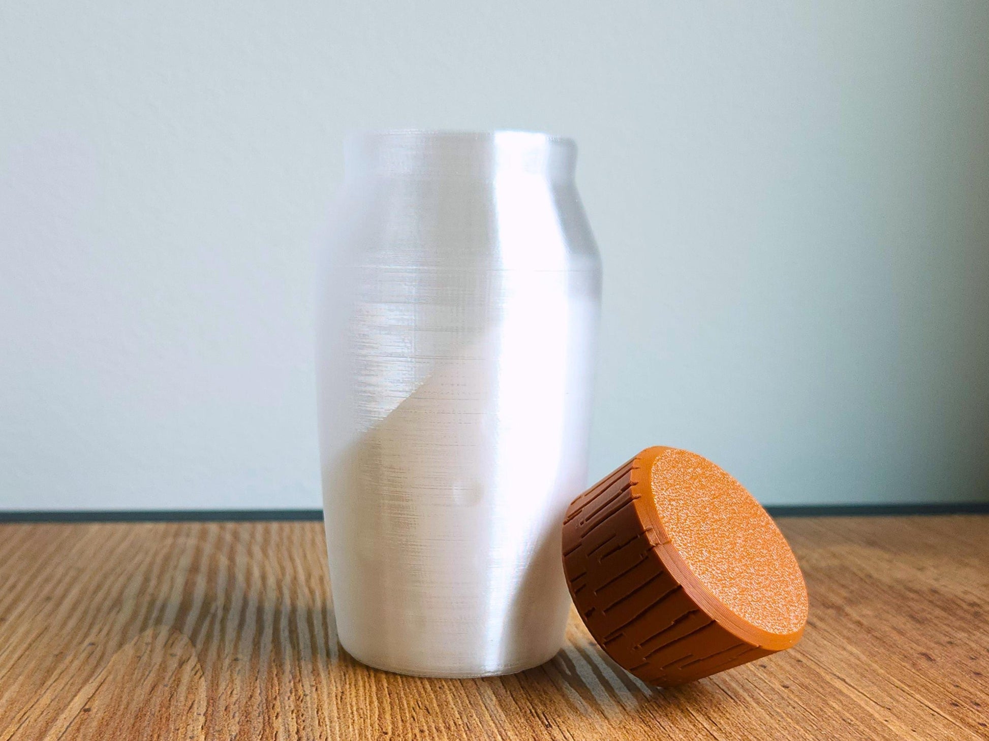 A 3D-printed potion bottle and a separate brown wood-textured cap resting on a wooden surface, displayed against a clean white background.