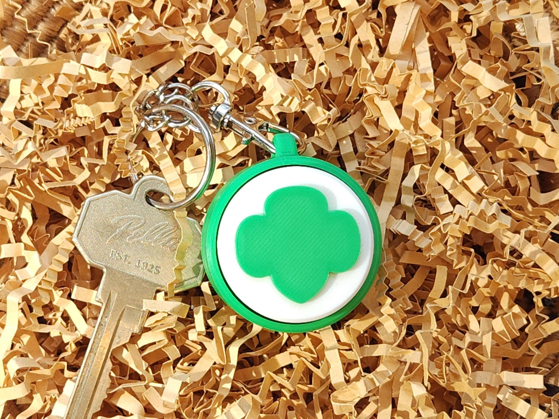 Close-up of the clicker keychain on brown crinkle paper, showing the trefoil design clearly