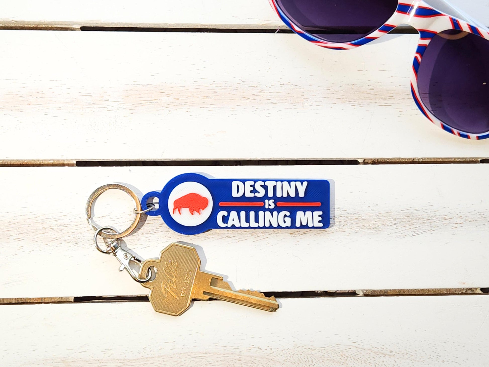 A blue keychain that says Destiny is Calling Me Go Bills with a red bison displayed alongside some accessories.