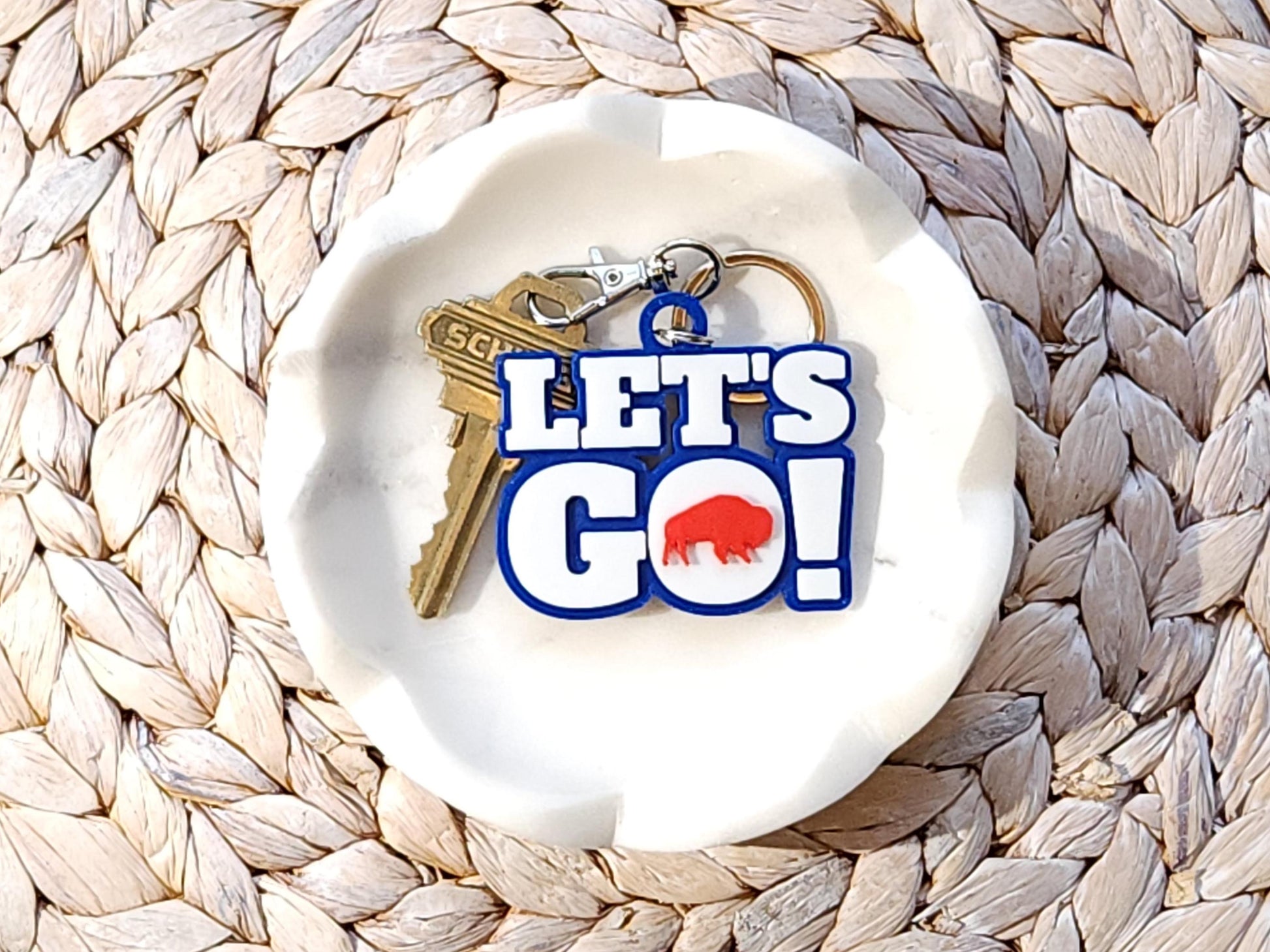 View of Let&#39;s Go Buffalo football keychain in a white dish on a woven background.