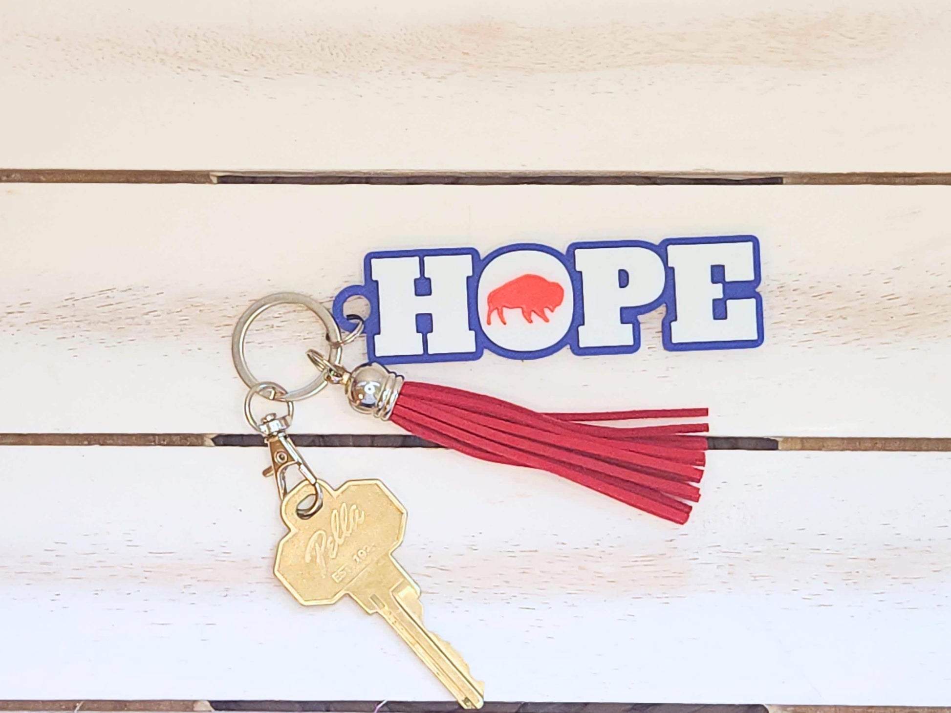 The “HOPE” keychain with red buffalo, attached to a red tassel and brass key, placed on a white wooden surface.