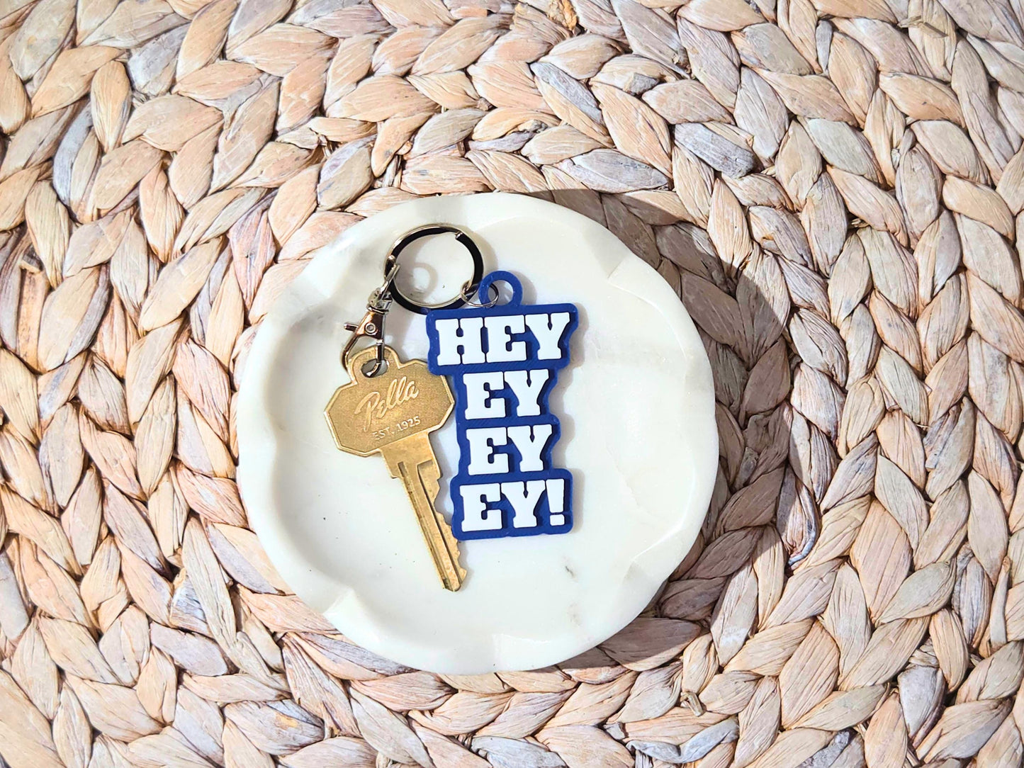 Buffalo football keychain featuring the phrase Hey Ey Ey Ey on a blue  background in a white marble dish.