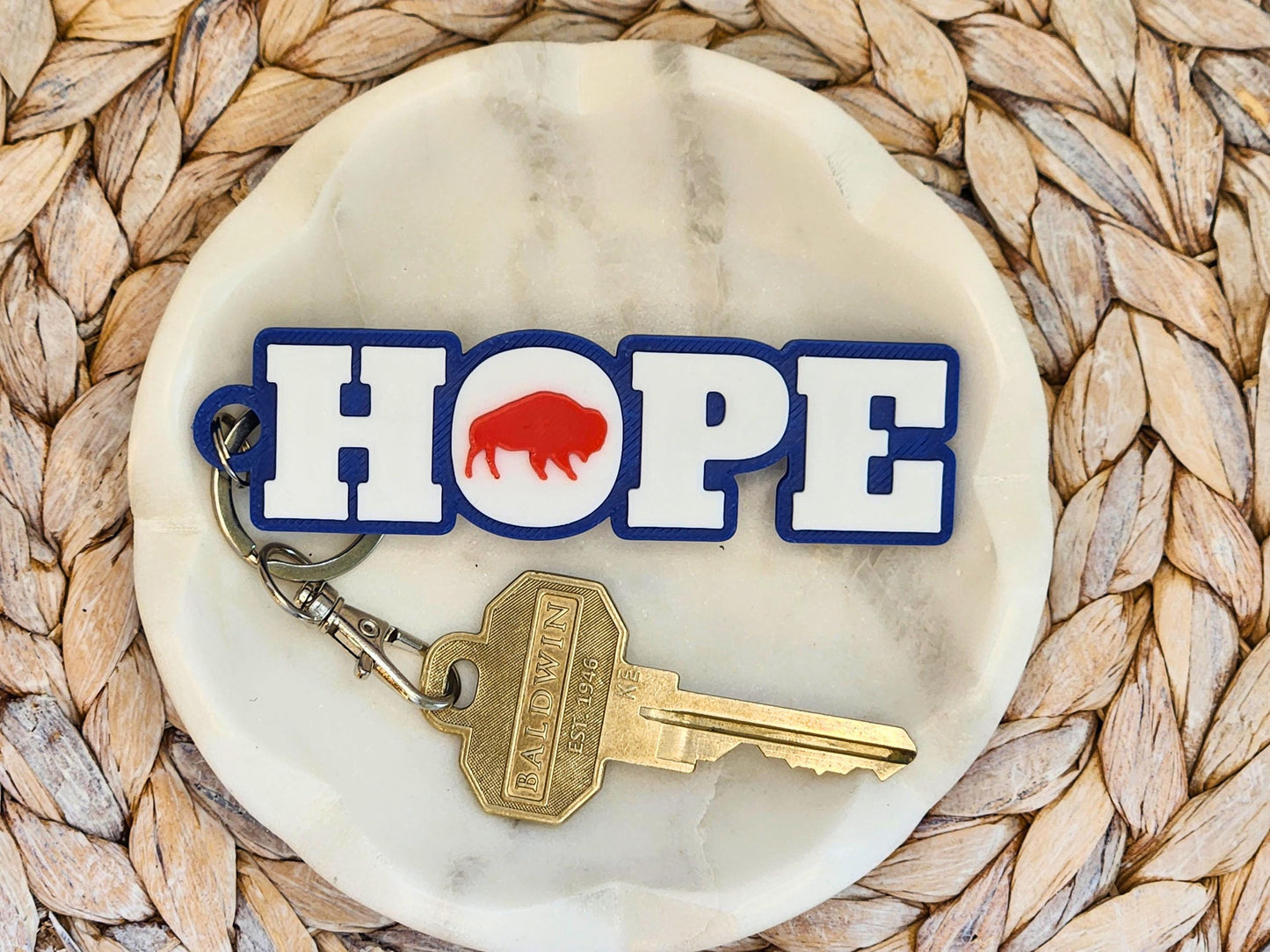 Buffalo football keychain with HOPE design, featuring red buffalo silhouette on white and blue lettering, displayed on a marble dish with a brass key.