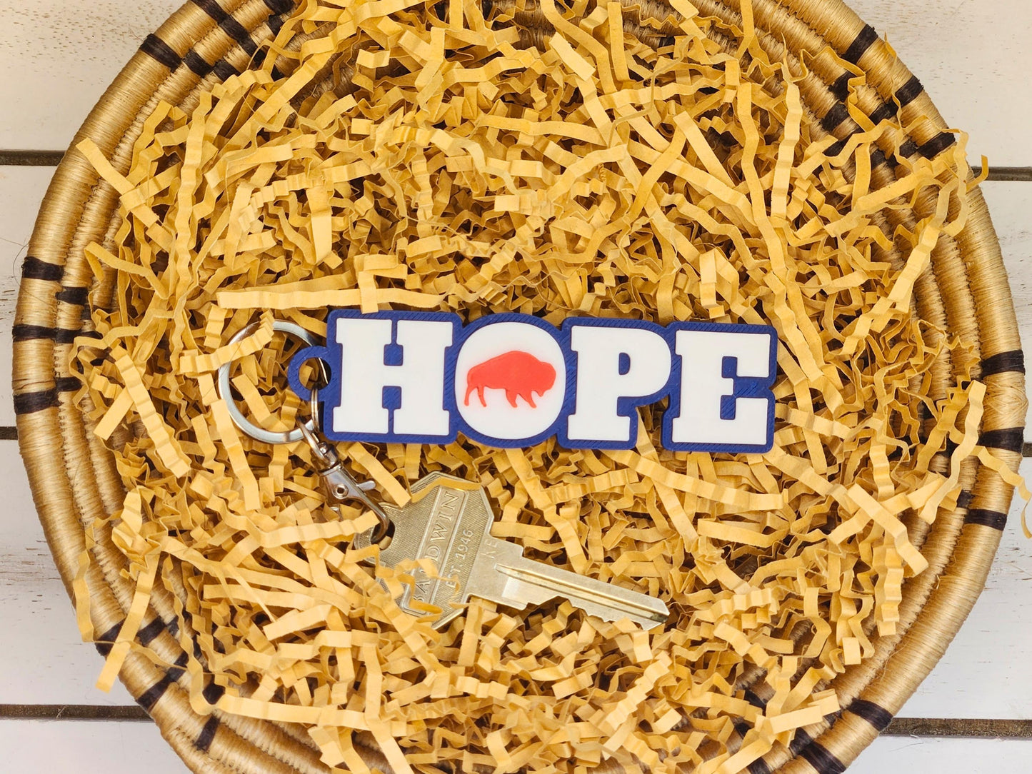 Close-up of the same keychain inside a round woven basket filled with crinkle paper, attached to a single brass key without the tassel.
