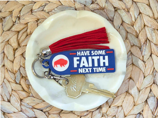 Close-up of 3D printed blue keychain with red tassel and gold key, displayed on a round white marble dish atop a woven placemat.