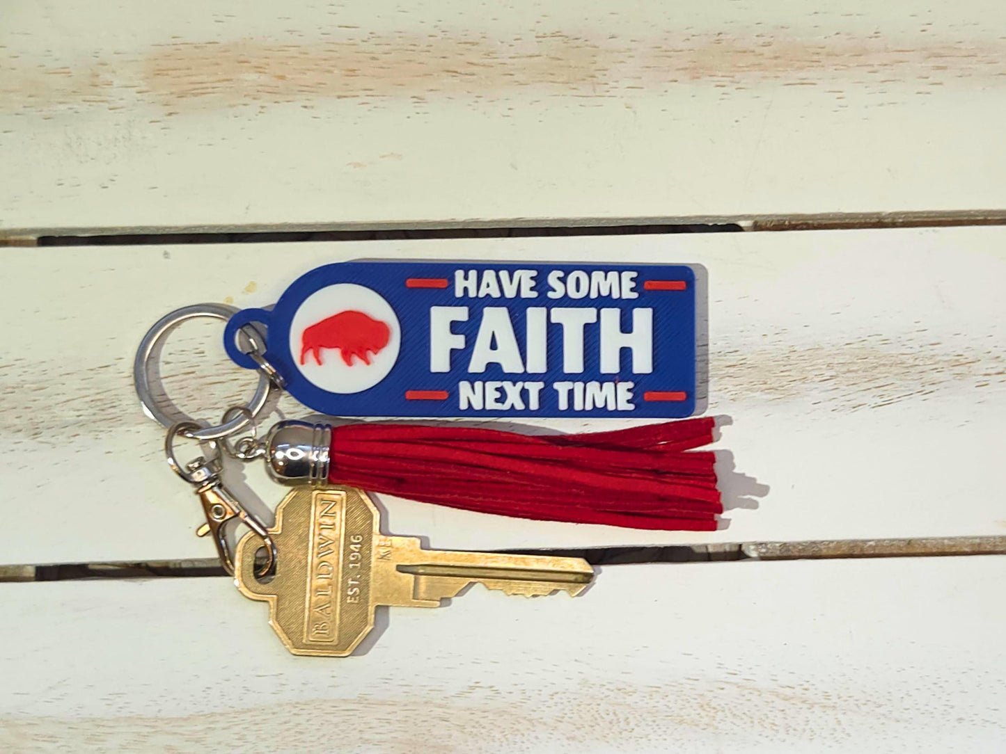 Blue 3D printed keychain with red tassel and gold keys, reading &#39;Have Some Faith Next Time,&#39; styled on a white wood background.