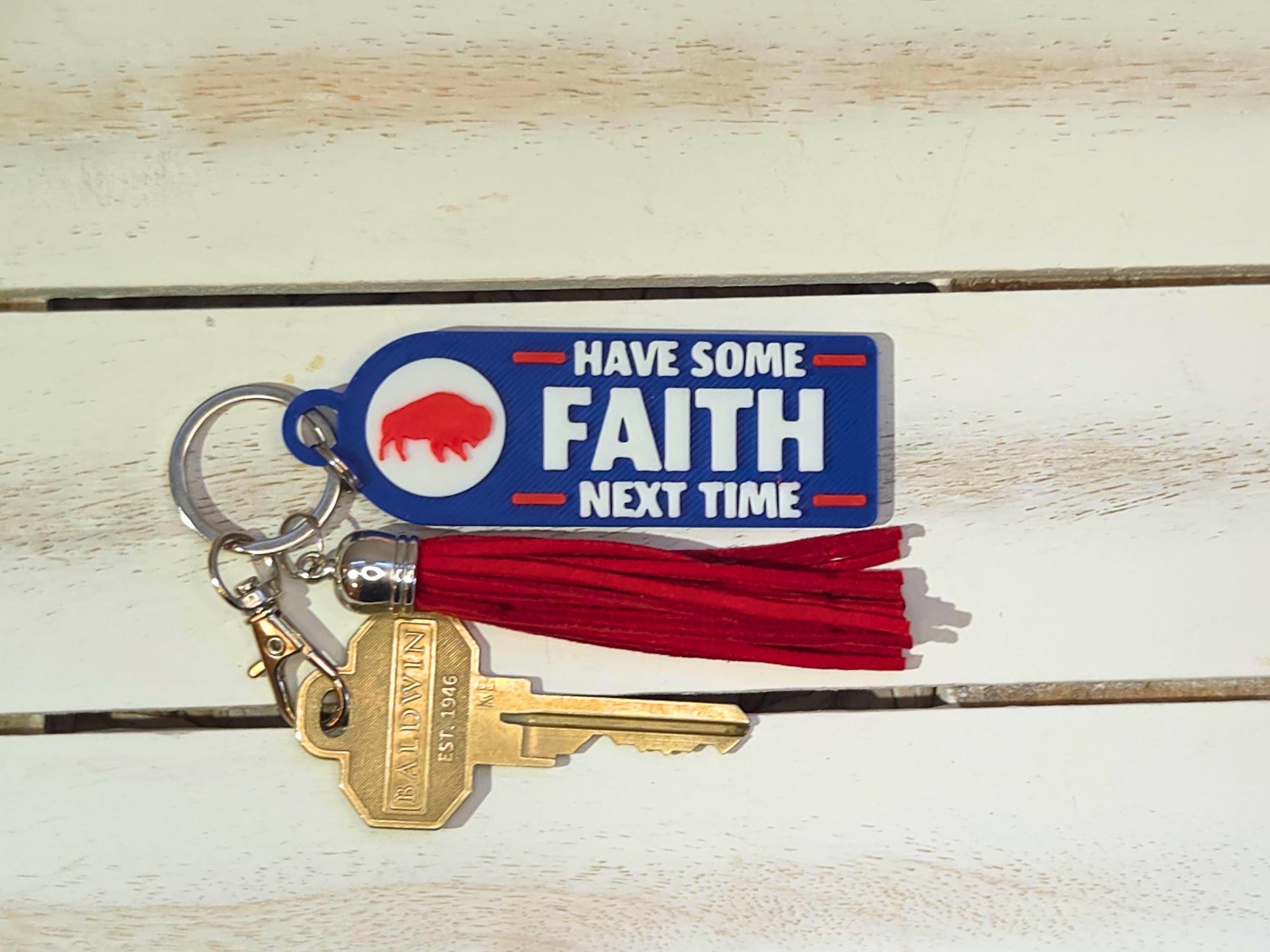 Blue 3D printed keychain with red tassel and gold keys, reading &#39;Have Some Faith Next Time,&#39; styled on a white wood background.