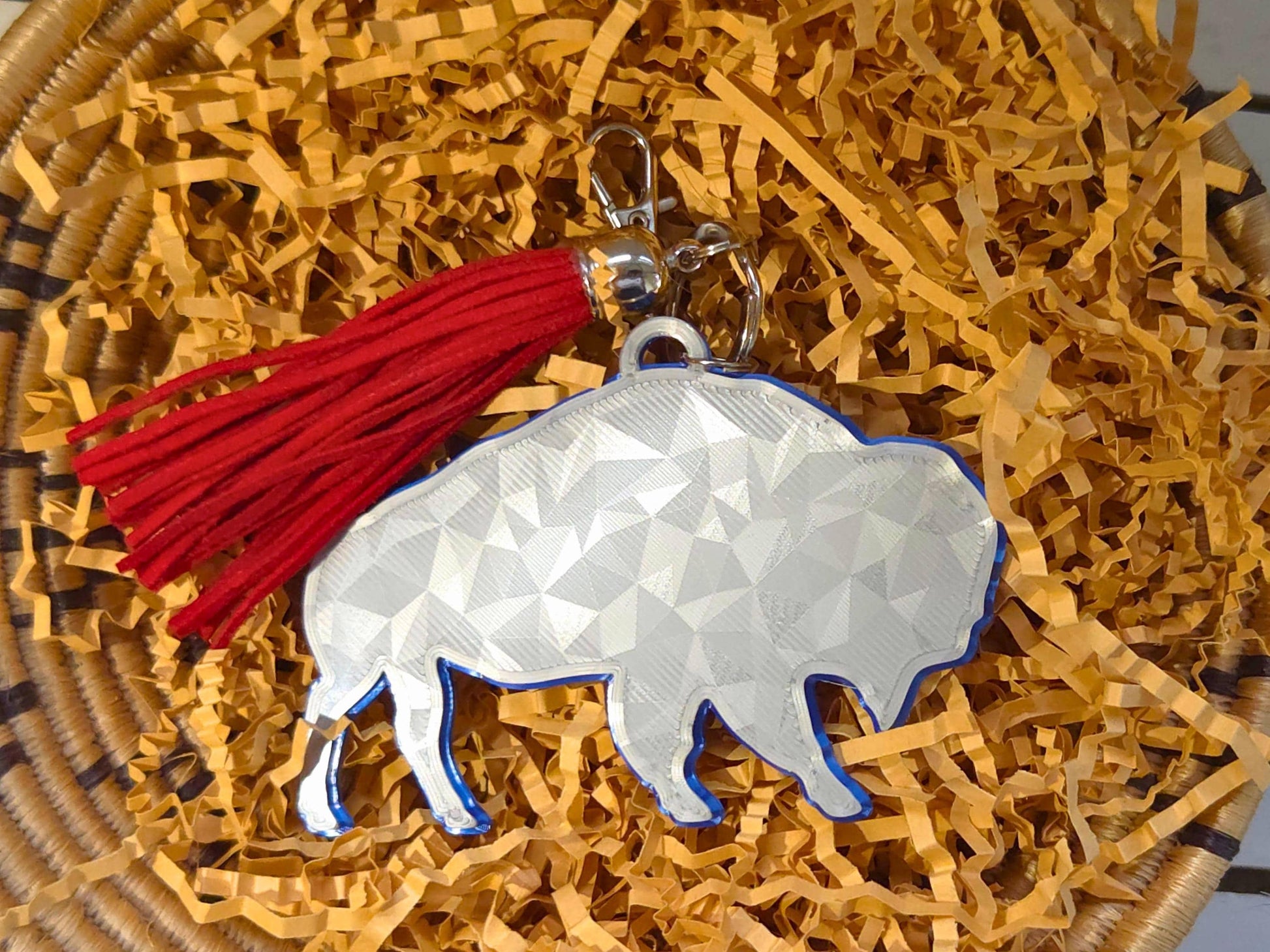 3D printed buffalo bag charm in icy white with red tassel, displayed in eco-friendly crinkle paper – perfect purse or backpack accessory for football fans.