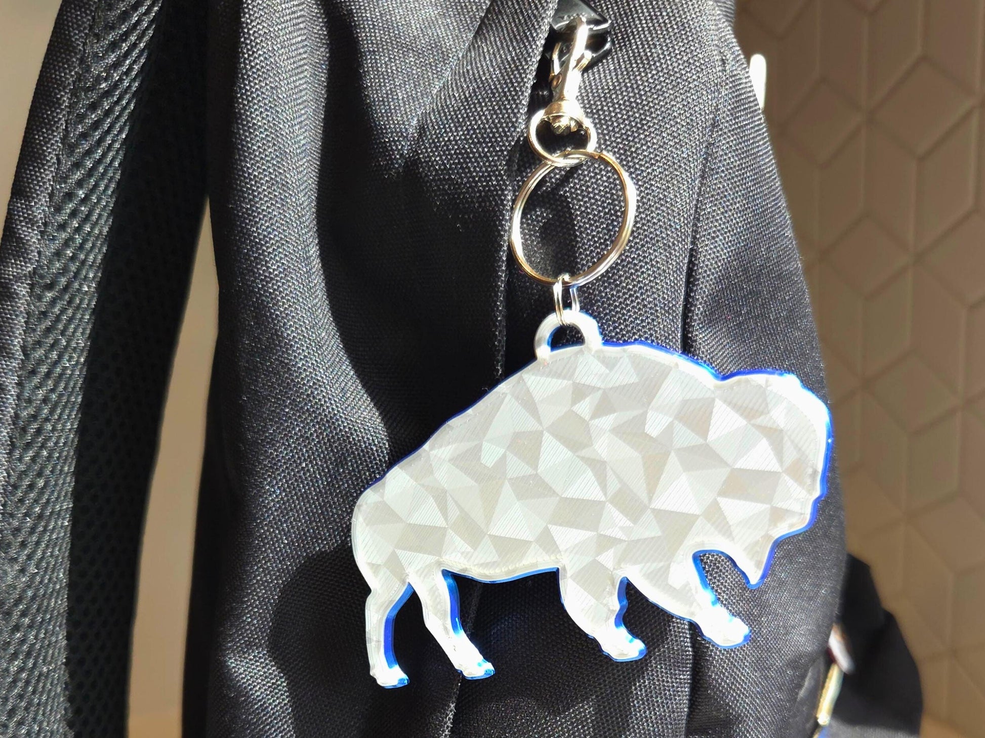 Buffalo football standing bison logo with geometric finish featured as a backpack charm in silver with a blue backing, and a red tassel for contrast.