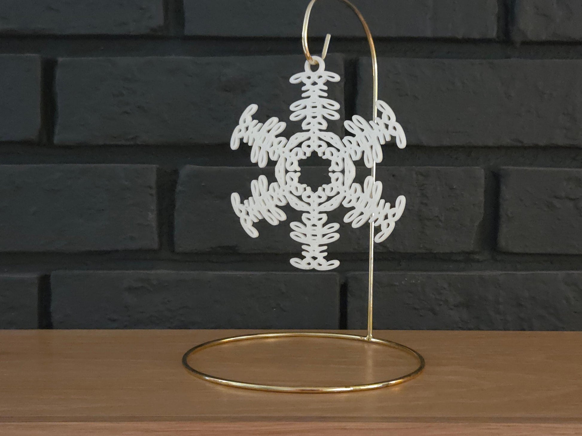 White snowflake christmas ornament that spells the word &quot;Buffalo&quot; hanging on a gold display hook in front of a black brick background.