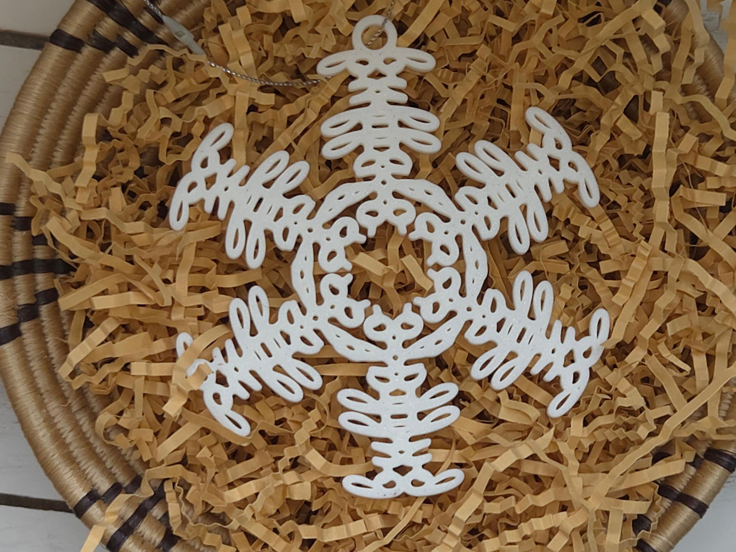 White snowflake christmas ornament that spells the word &quot;Buffalo&quot; displayed in craft paper in a basket on a wooden background.