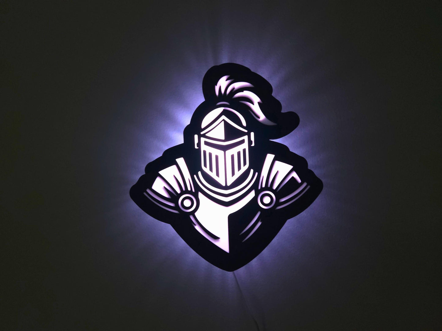 The knight lamp is illuminated in white on a wall with the lights off.