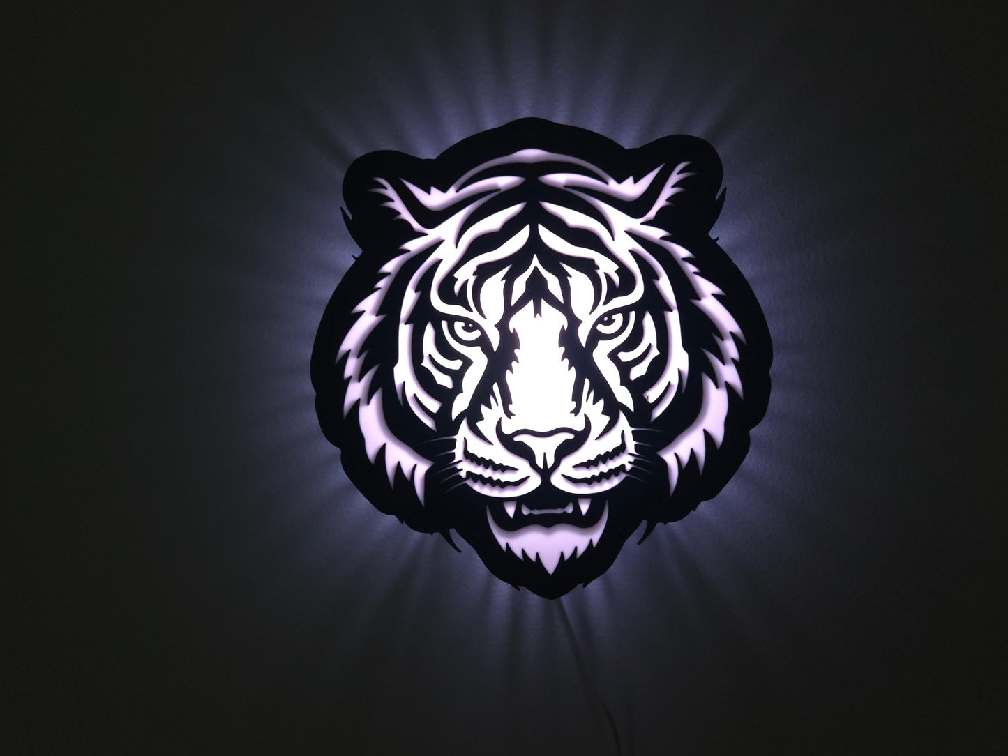 The tiger lamp is illuminated in white on a wall with the lights off.
