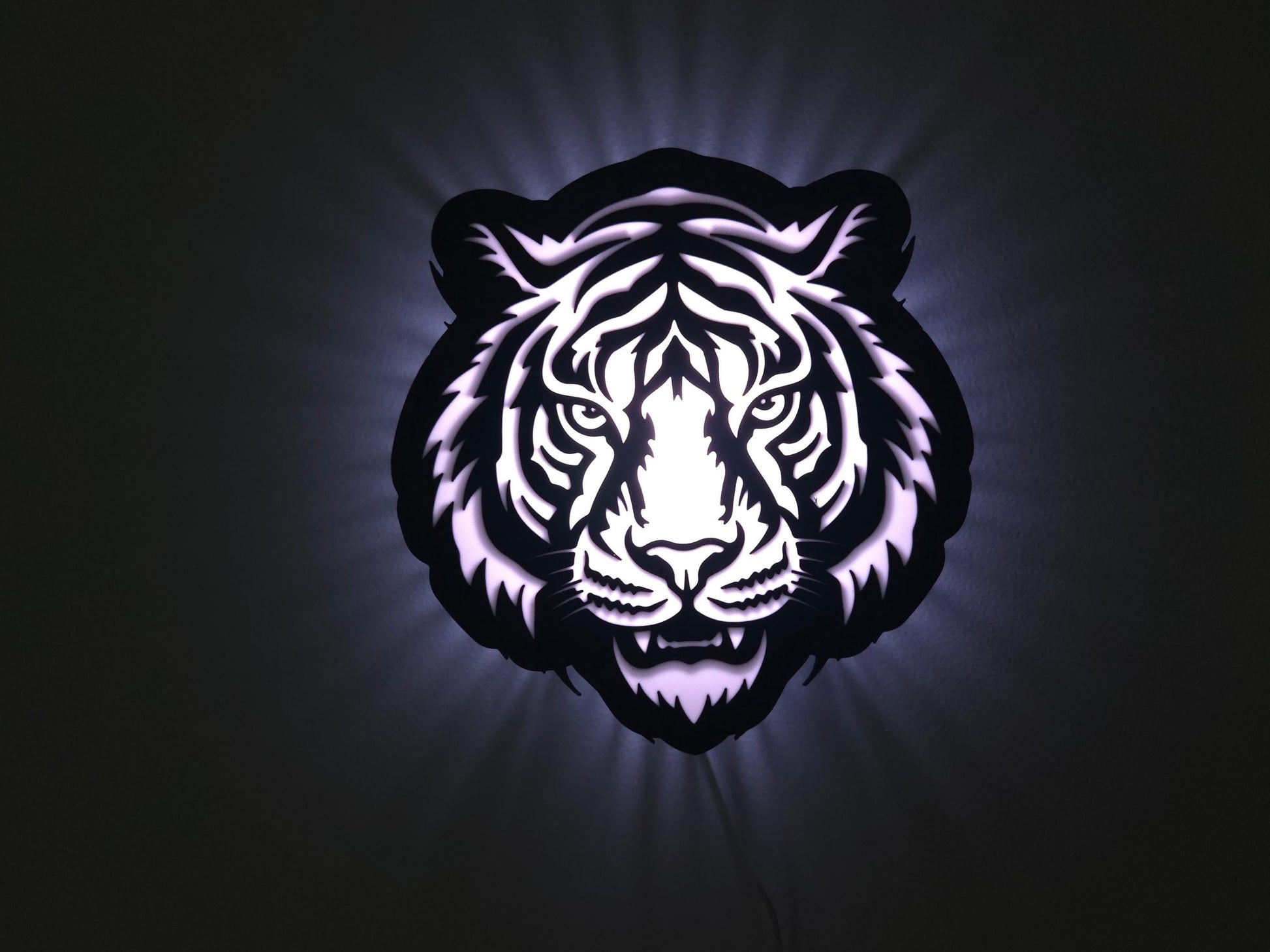 The tiger lamp is illuminated in white on a wall with the lights off.