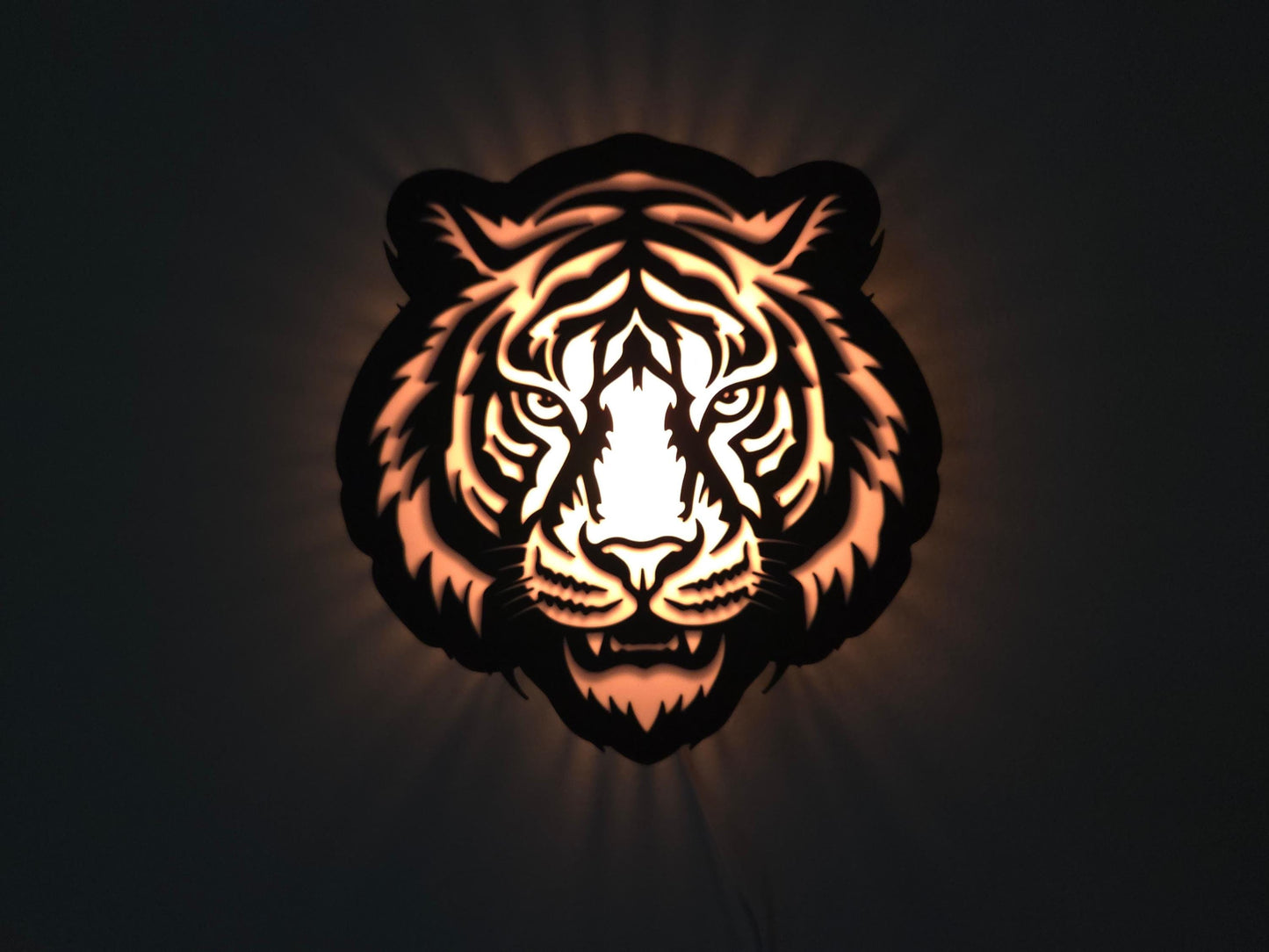 The tiger lamp is illuminated in orange on a wall with the lights off.