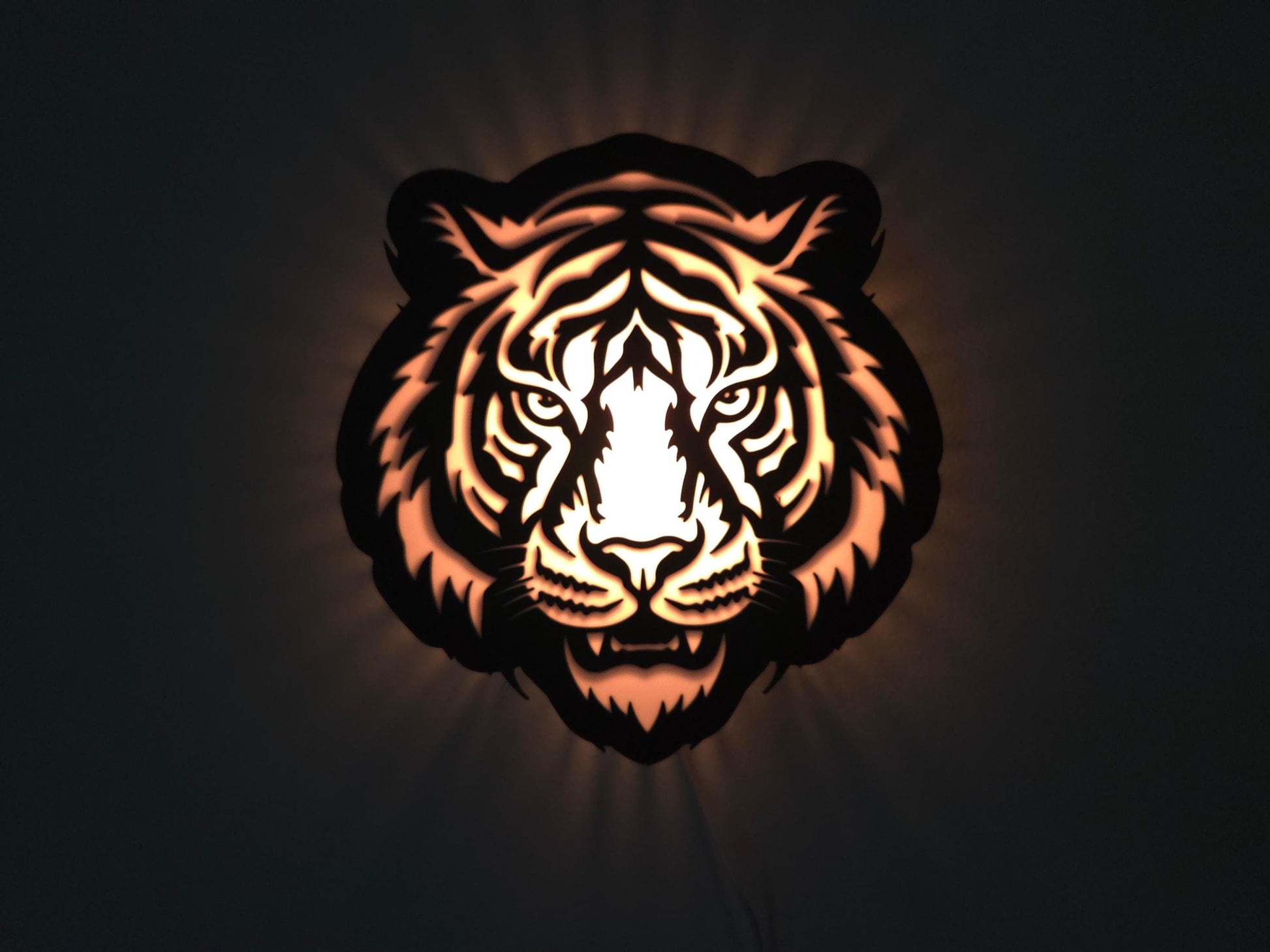The tiger lamp is illuminated in orange on a wall with the lights off.