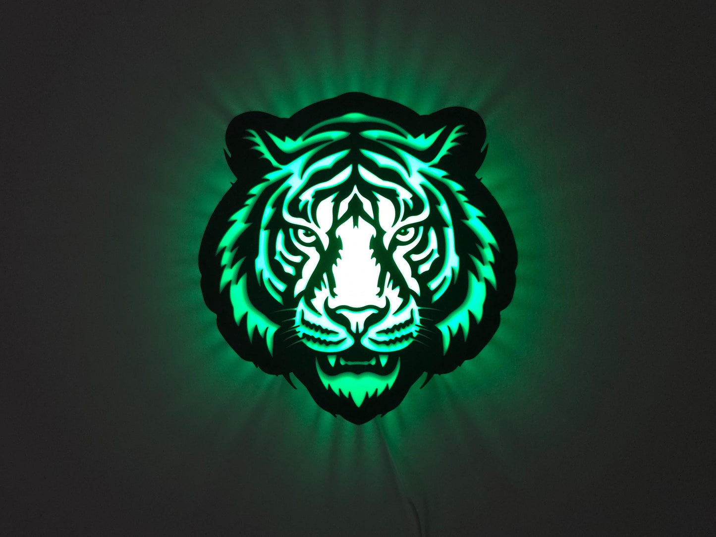 The tiger lamp is illuminated in green on a wall with the lights off.