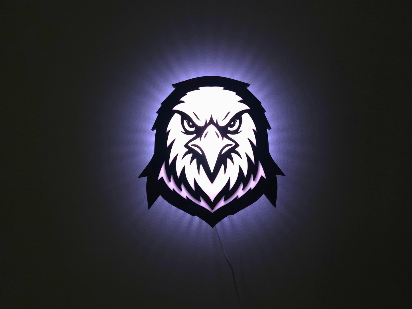 The eagle, hawk or falcon lamp is illuminated in white on a wall with the lights off.