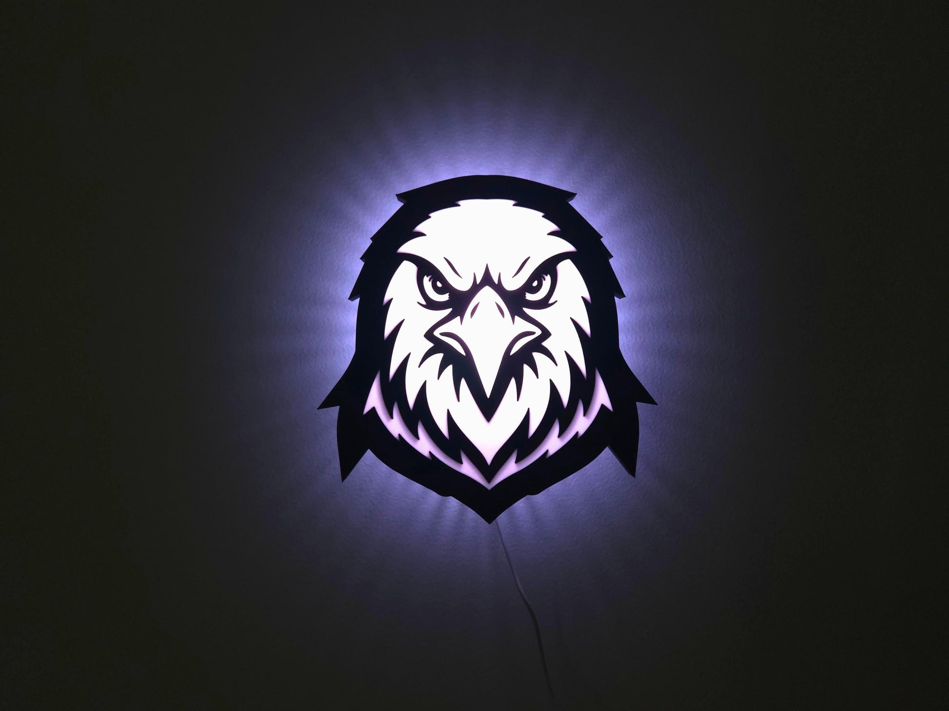 The eagle, hawk or falcon lamp is illuminated in white on a wall with the lights off.