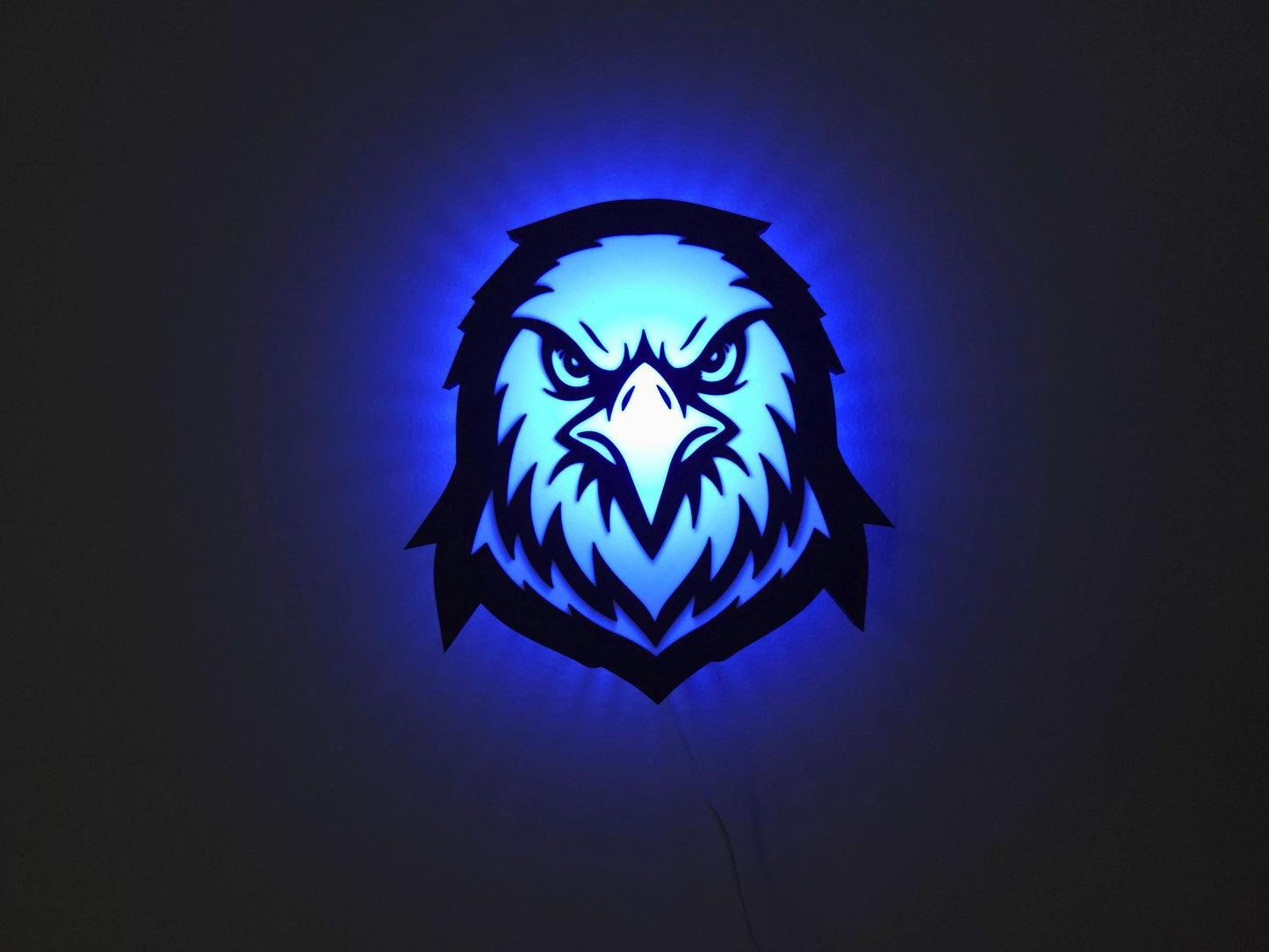 The eagle, hawk or falcon lamp is illuminated in blue on a wall with the lights off.