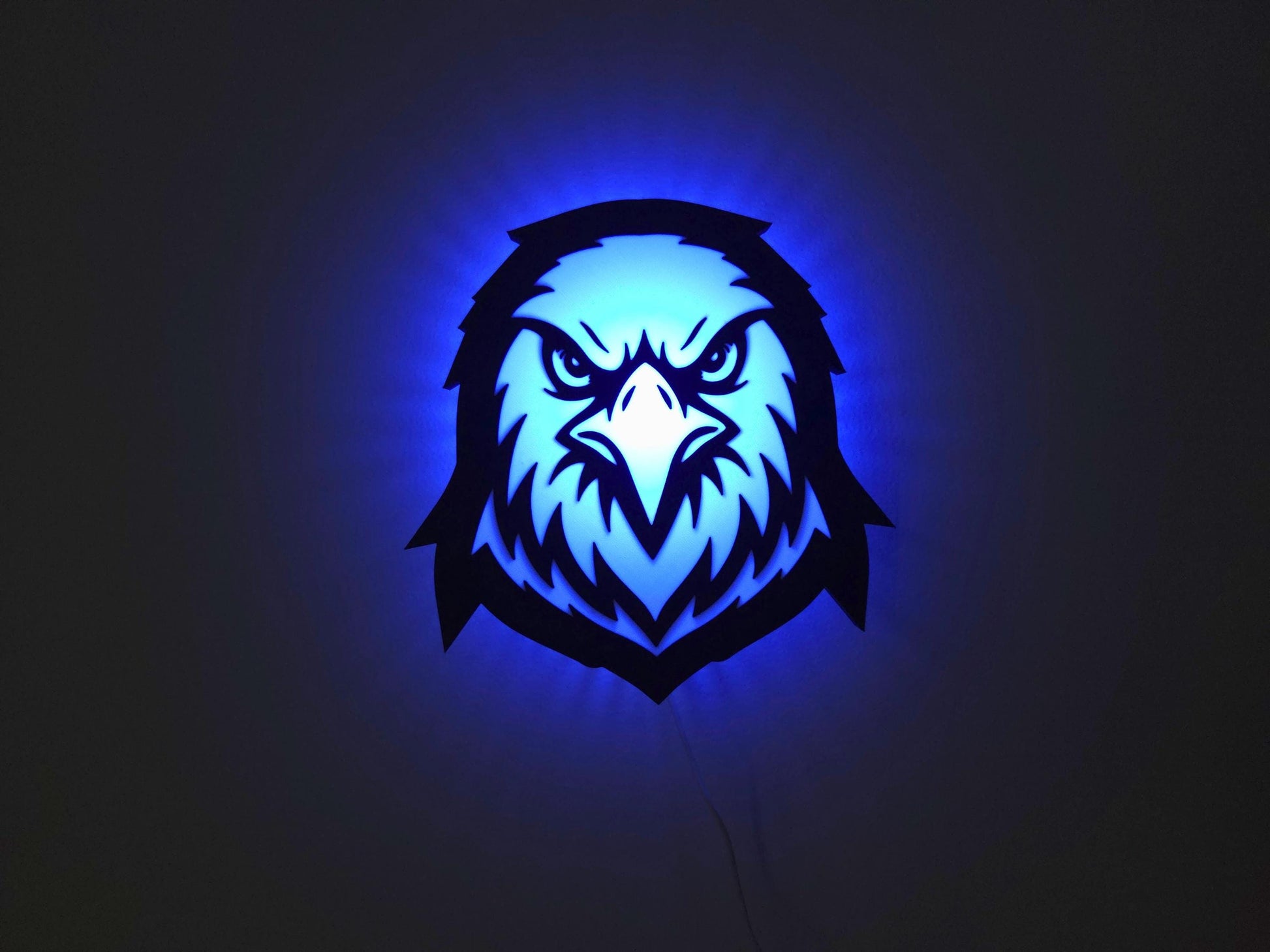 The eagle, hawk or falcon lamp is illuminated in blue on a wall with the lights off.
