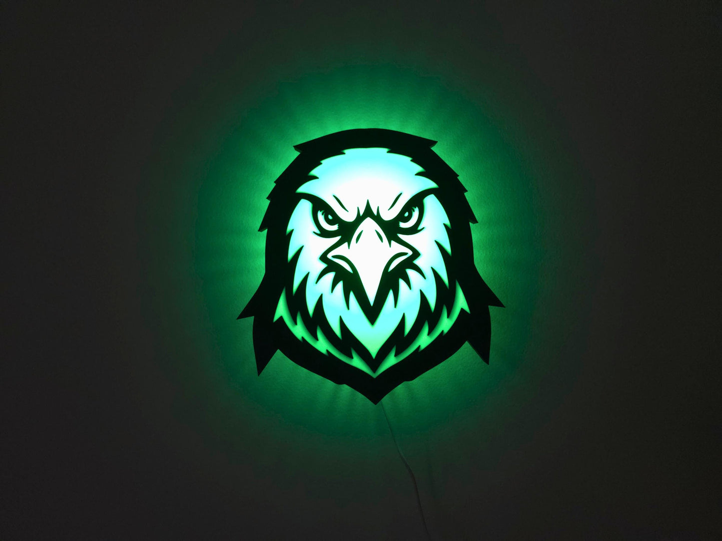 The eagle, hawk or falcon lamp is illuminated in green on a wall with the lights off.