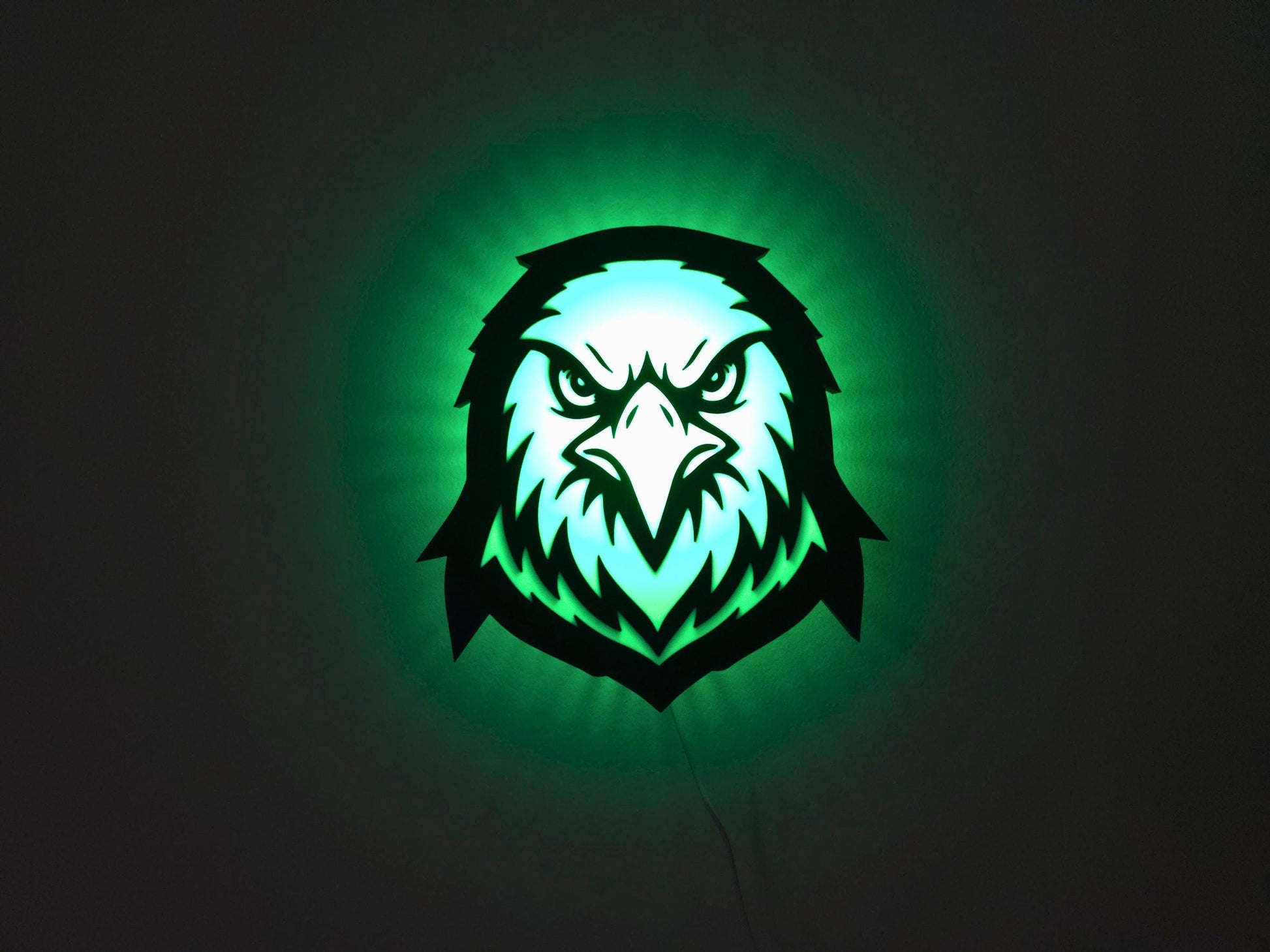 The eagle, hawk or falcon lamp is illuminated in green on a wall with the lights off.