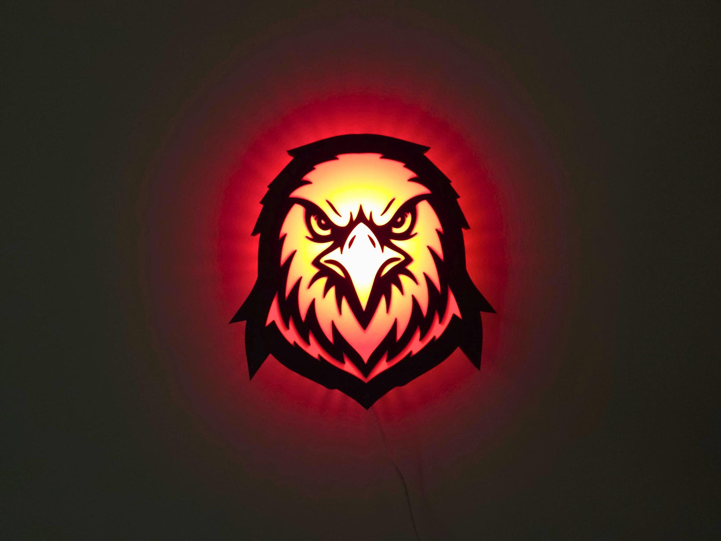 The eagle, hawk or falcon lamp is illuminated in red on a wall with the lights off.