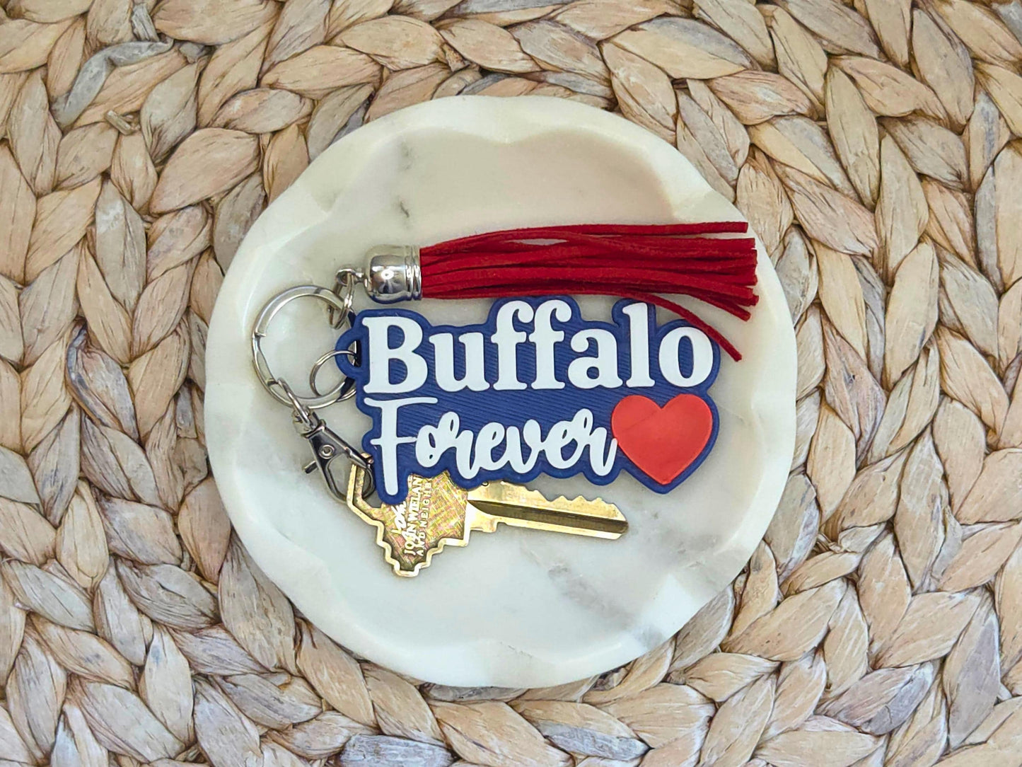 Buffalo Forever keychain featured in a white dish on a woven background with a red tassel. A key is shown for scale.