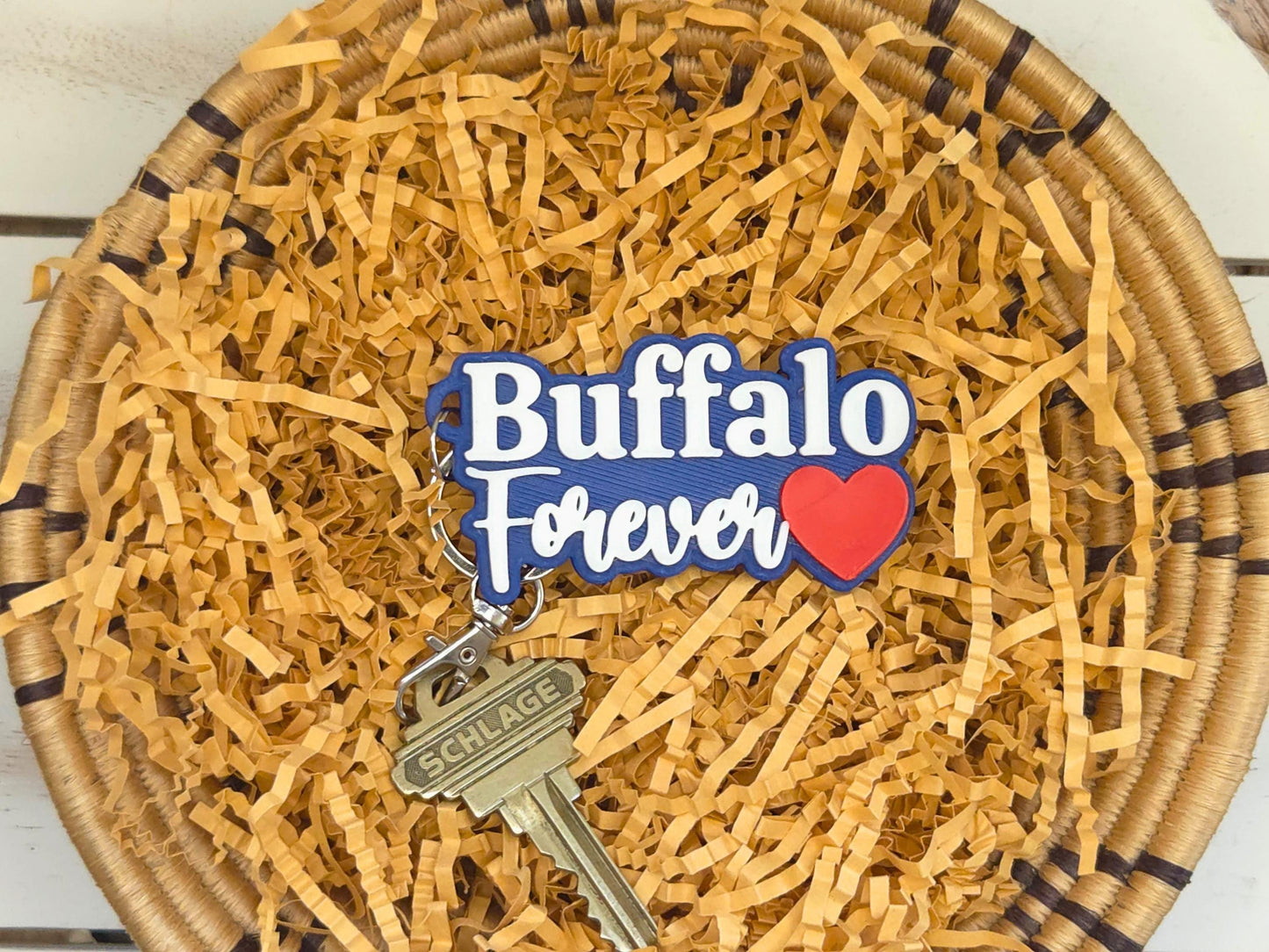 Buffalo Forever keychain featured in kraft paper on a wooden background.  A key is shown for scale.