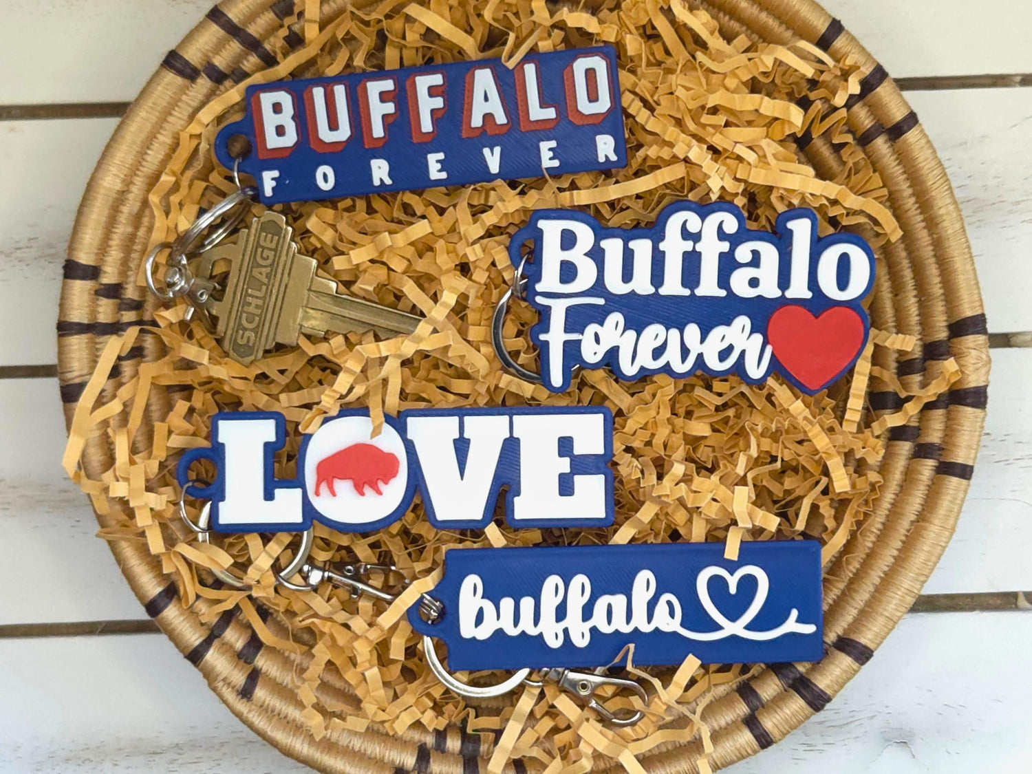 All four new keychains are shown: Buffalo Forever in block letters, Buffalo Forever in script letters, Buffalo Love, and Buffalo heart in kraft paper on a wooden background.