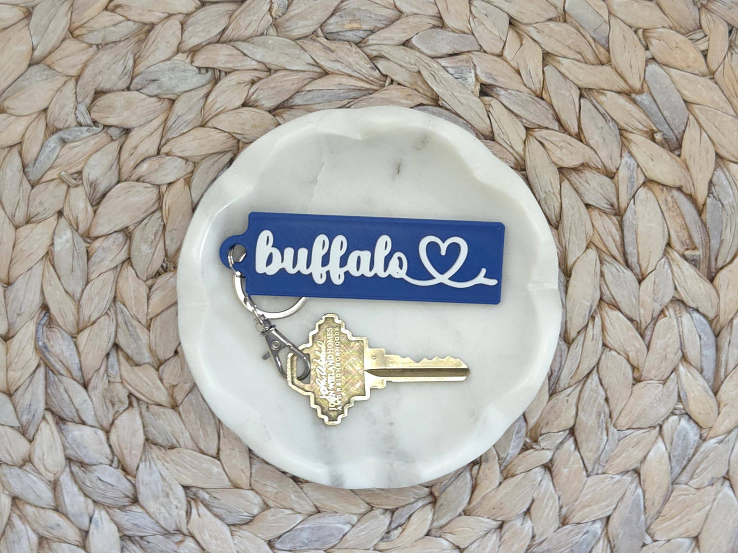 Buffalo heart keychain is featured in a white dish on a woven background. A key is shown for scale.