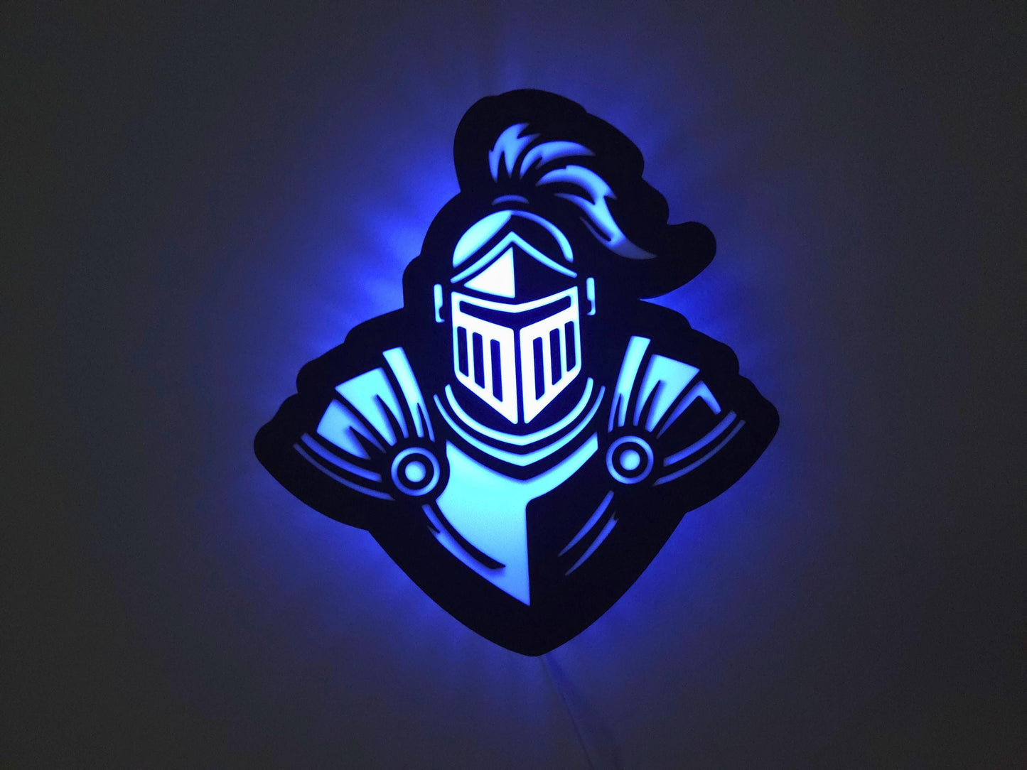 The knight lamp is illuminated in blue on a wall with the lights off.