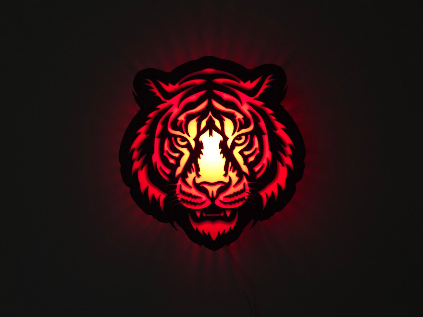 The tiger lamp is illuminated in red on a wall with the lights off.