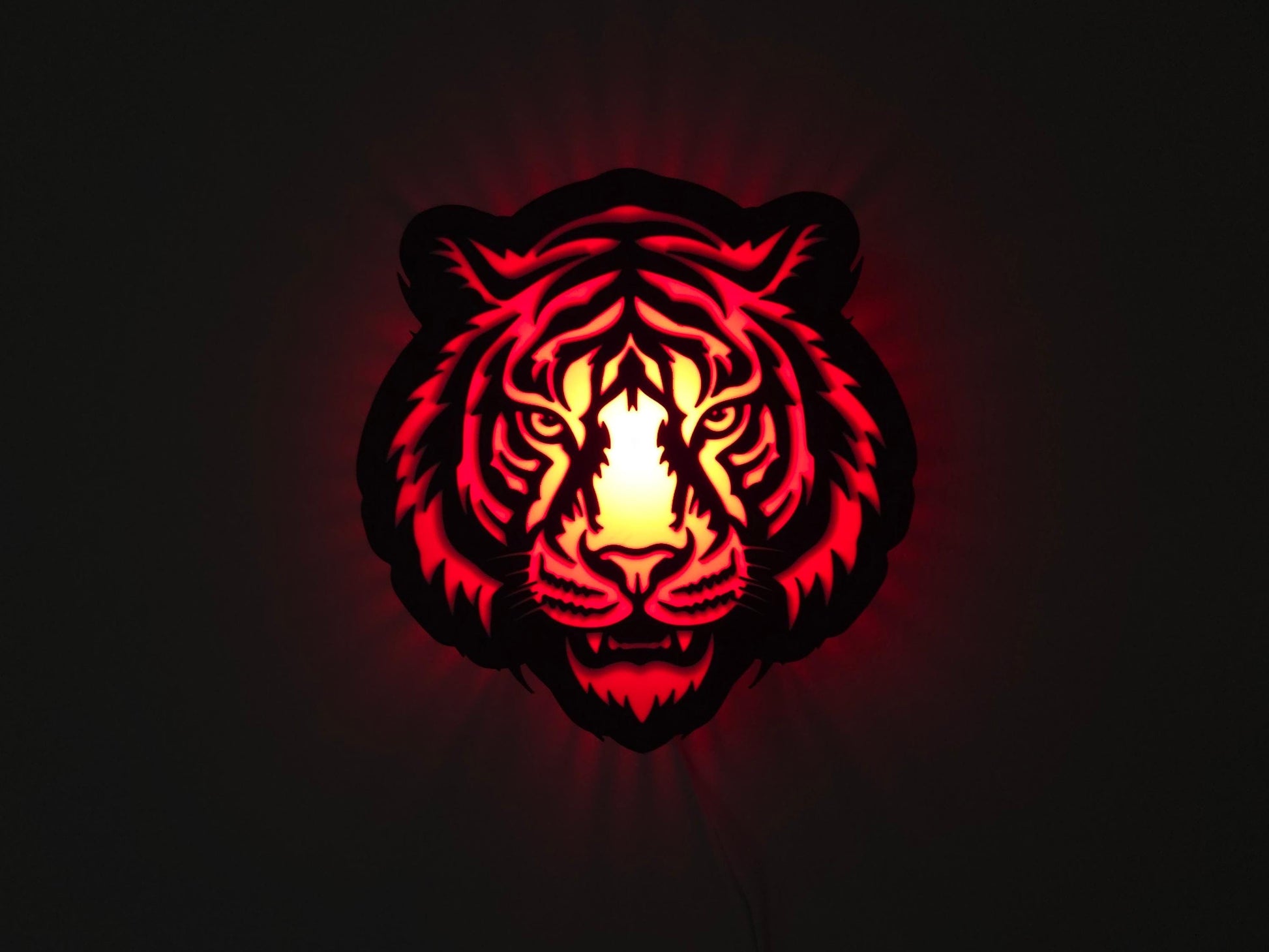 The tiger lamp is illuminated in red on a wall with the lights off.