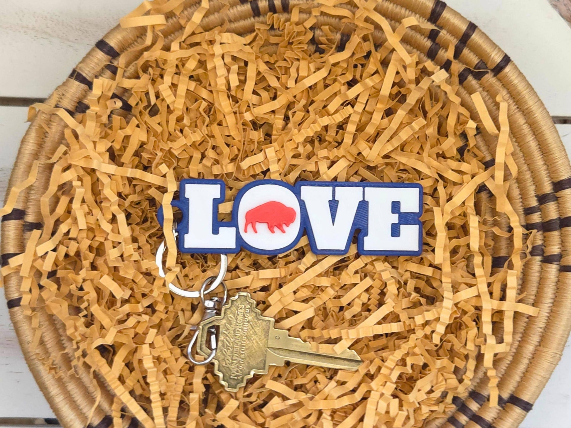 Buffalo Love Keychain or bag tag is shown in a basket with kraft paper on a wooden background. A key is shown for scale.