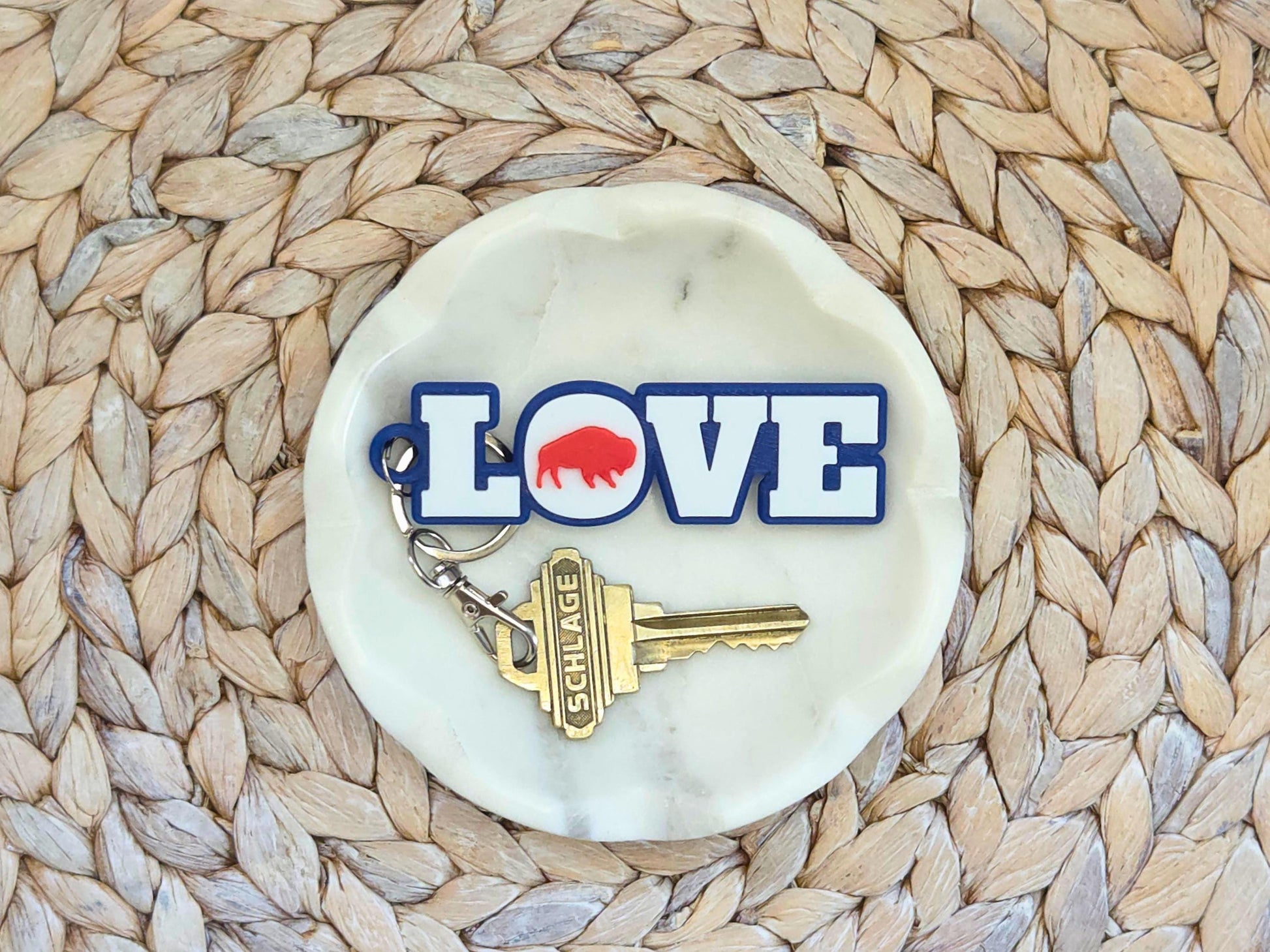 Buffalo Love Keychain or bag tag is shown in a white dish on a woven background. A key is shown for scale.