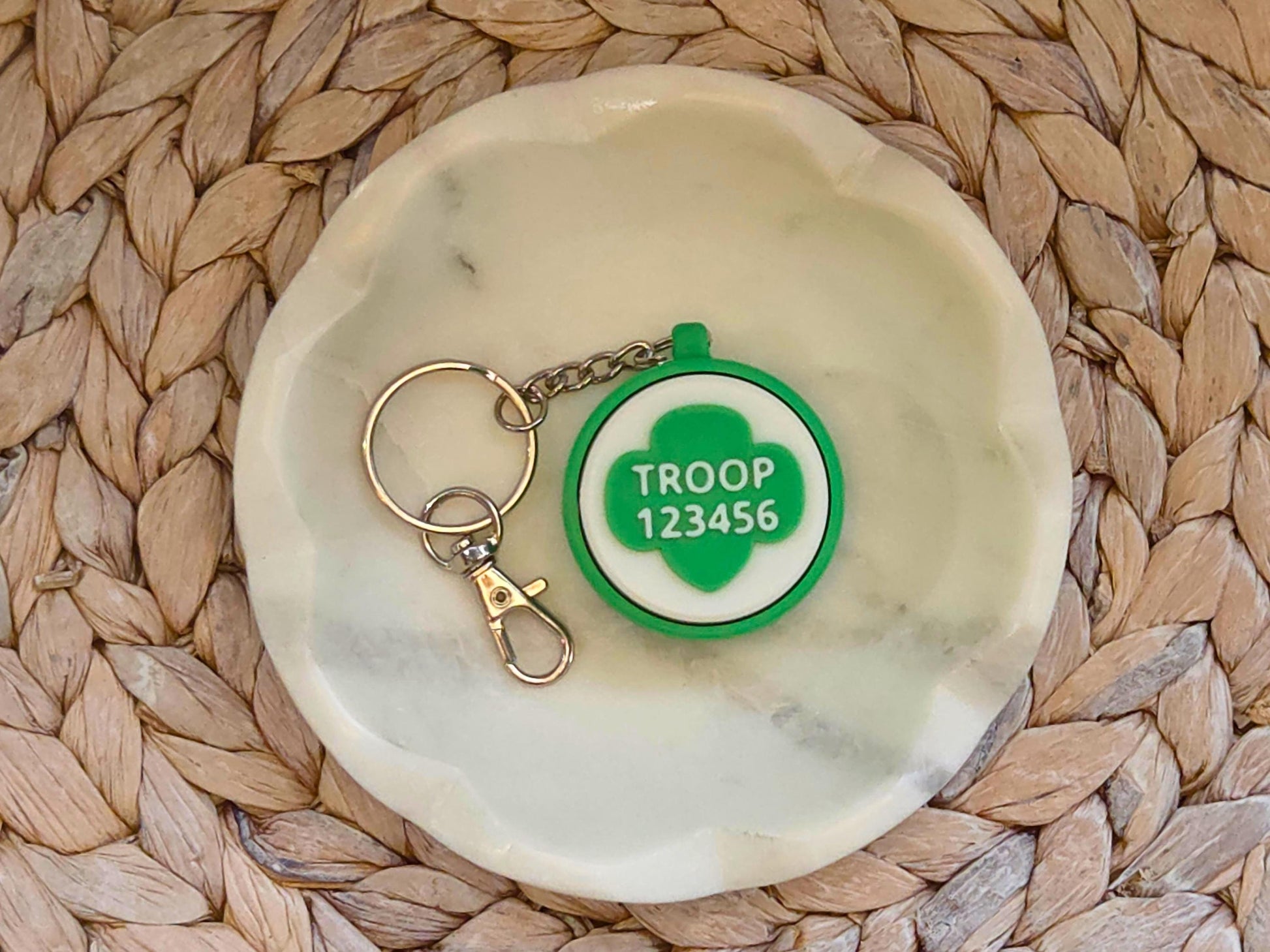 Green and white scout fidget clicker keychain personalized with the troop number 12345 is shown in a white dish on a woven background.