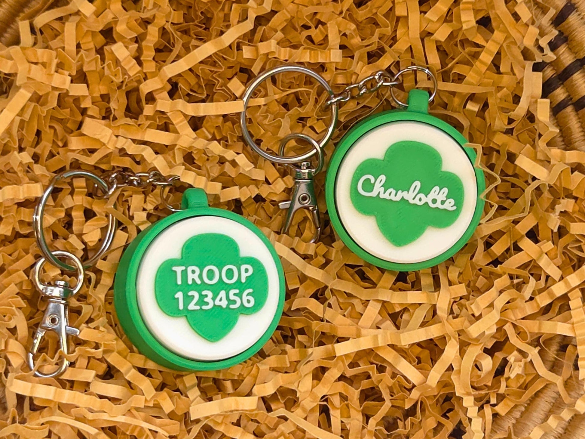 Two green and white scout fidget clicker keychains are shown in kraft paper. One is personalized with the name Charlotte and the other is personalized with troop number 12345.