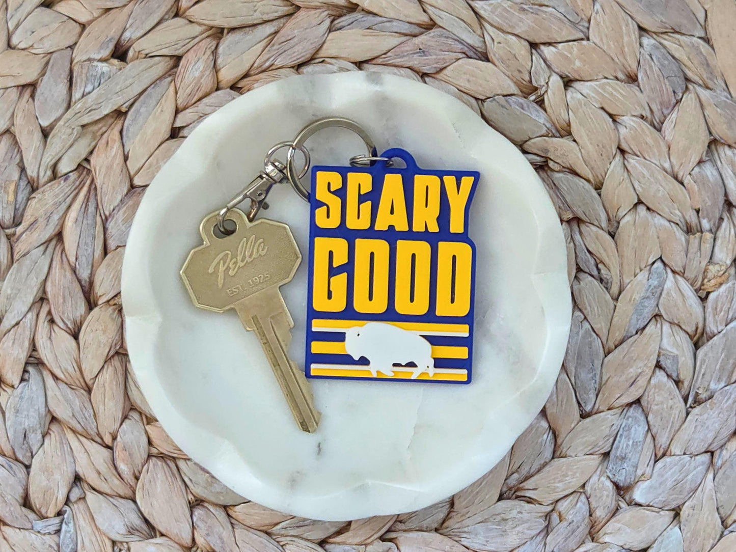 Blue and yellow Buffalo hockey keychain with "SCARY GOOD" text and bison logo on a white marble jewelry dish.