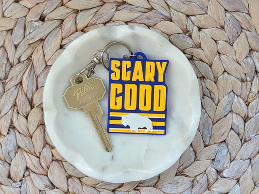 Blue and yellow Buffalo hockey keychain with "SCARY GOOD" text and bison logo on a white marble jewelry dish.