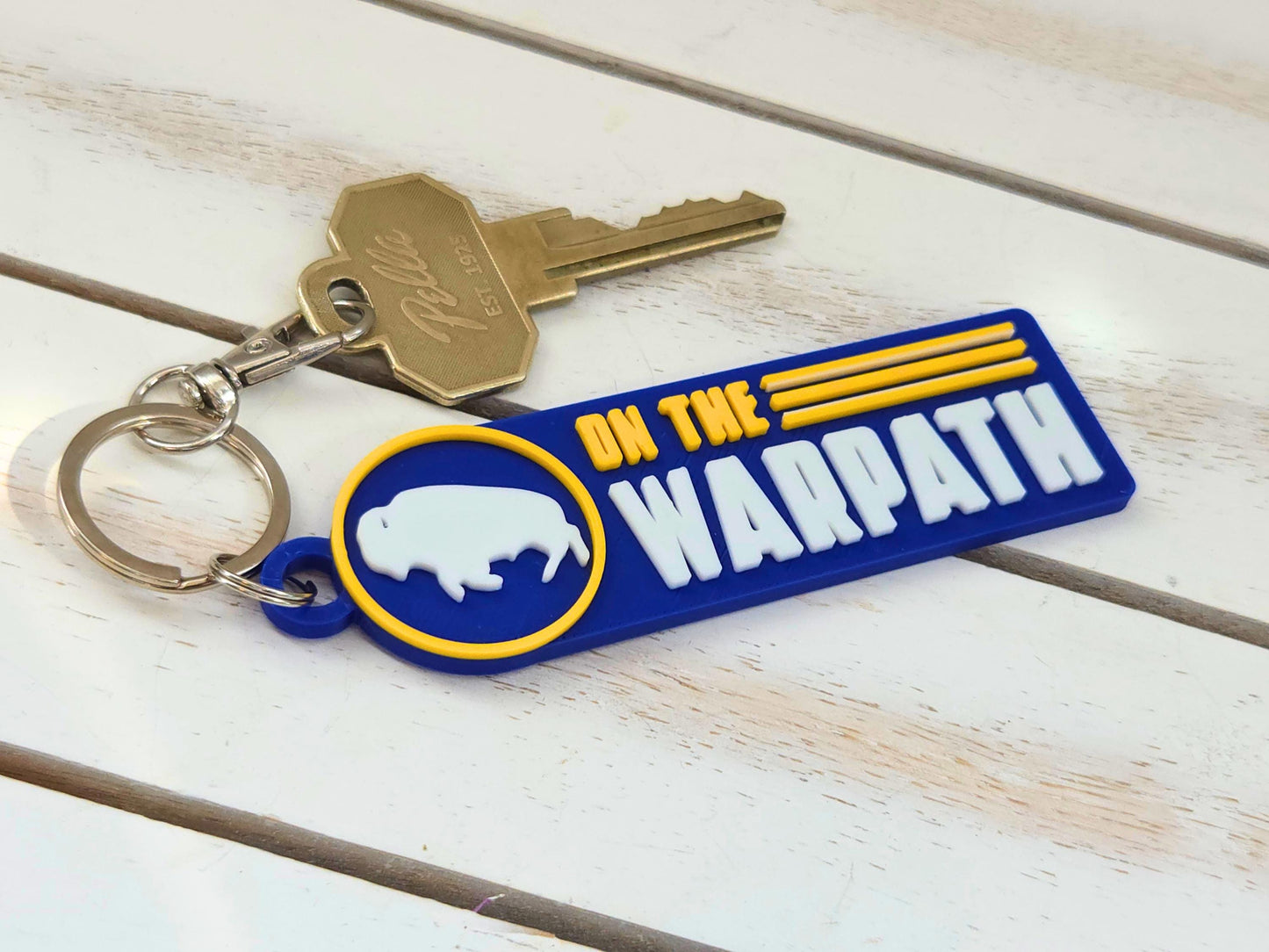 Buffalo "On the Warpath" hockey fan keychain with house key and quick-release clip on a white wood background.