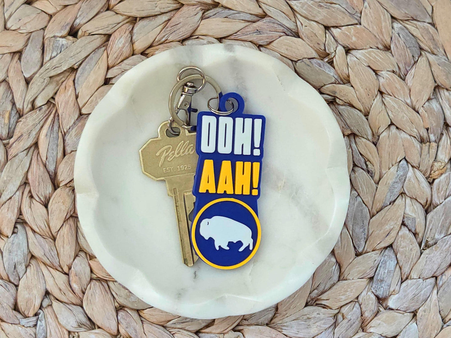 Blue and yellow 3D-printed Buffalo hockey keychain featuring "OOH! AAH!" text and bison logo on a white marble dish.