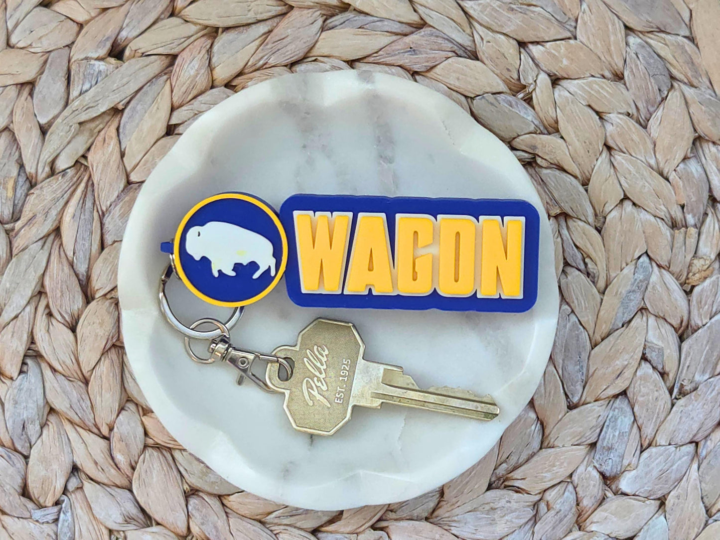 Chunky 3D-printed Buffalo hockey keychain with "WAGON" text and white bison logo in blue and yellow on a marble dish.