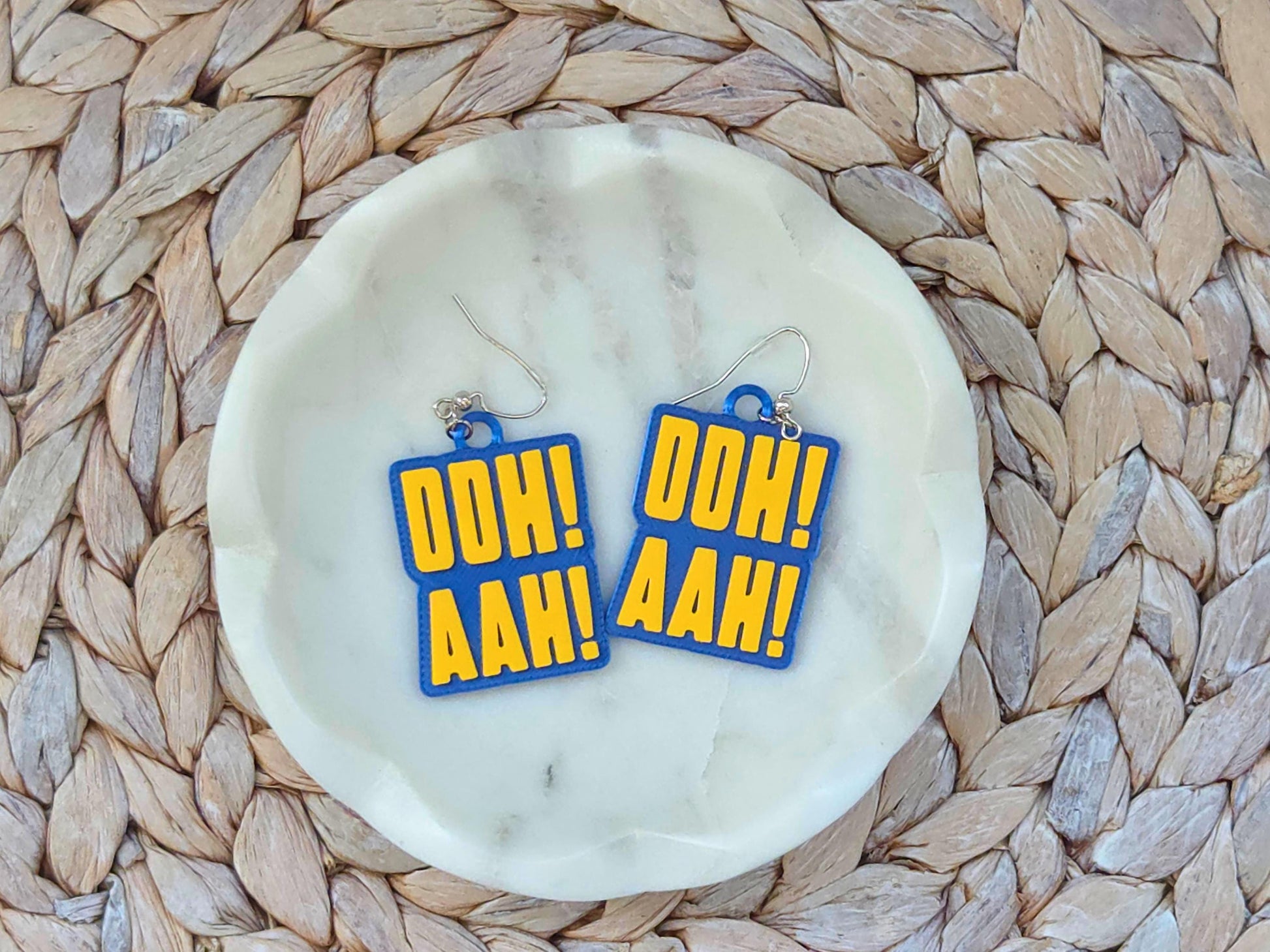 Pair of blue and yellow "OOH! AAH!" chant earrings for Buffalo hockey fans on a white marble jewelry dish.