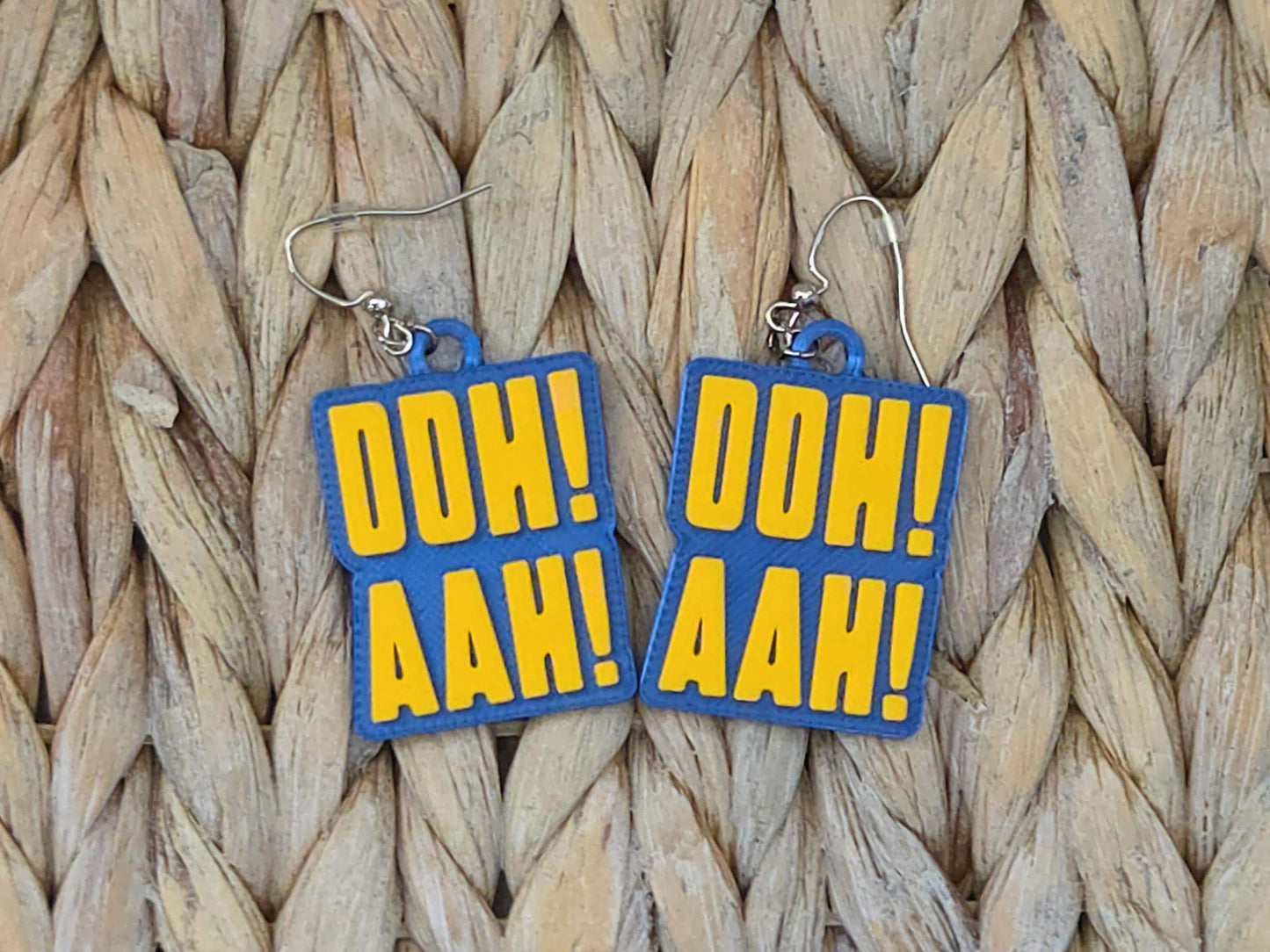 Close-up of 3D-printed textured plastic earrings with Buffalo team colors and chant text on a woven straw background.