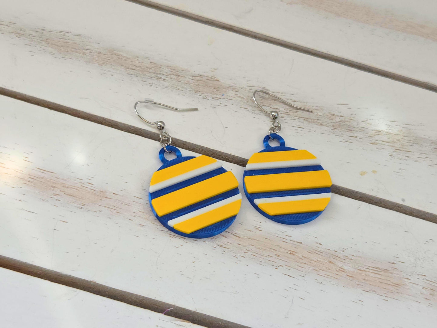 Lightweight blue and yellow striped dangle earrings with nickel-free hooks on a white shiplap wood surface.