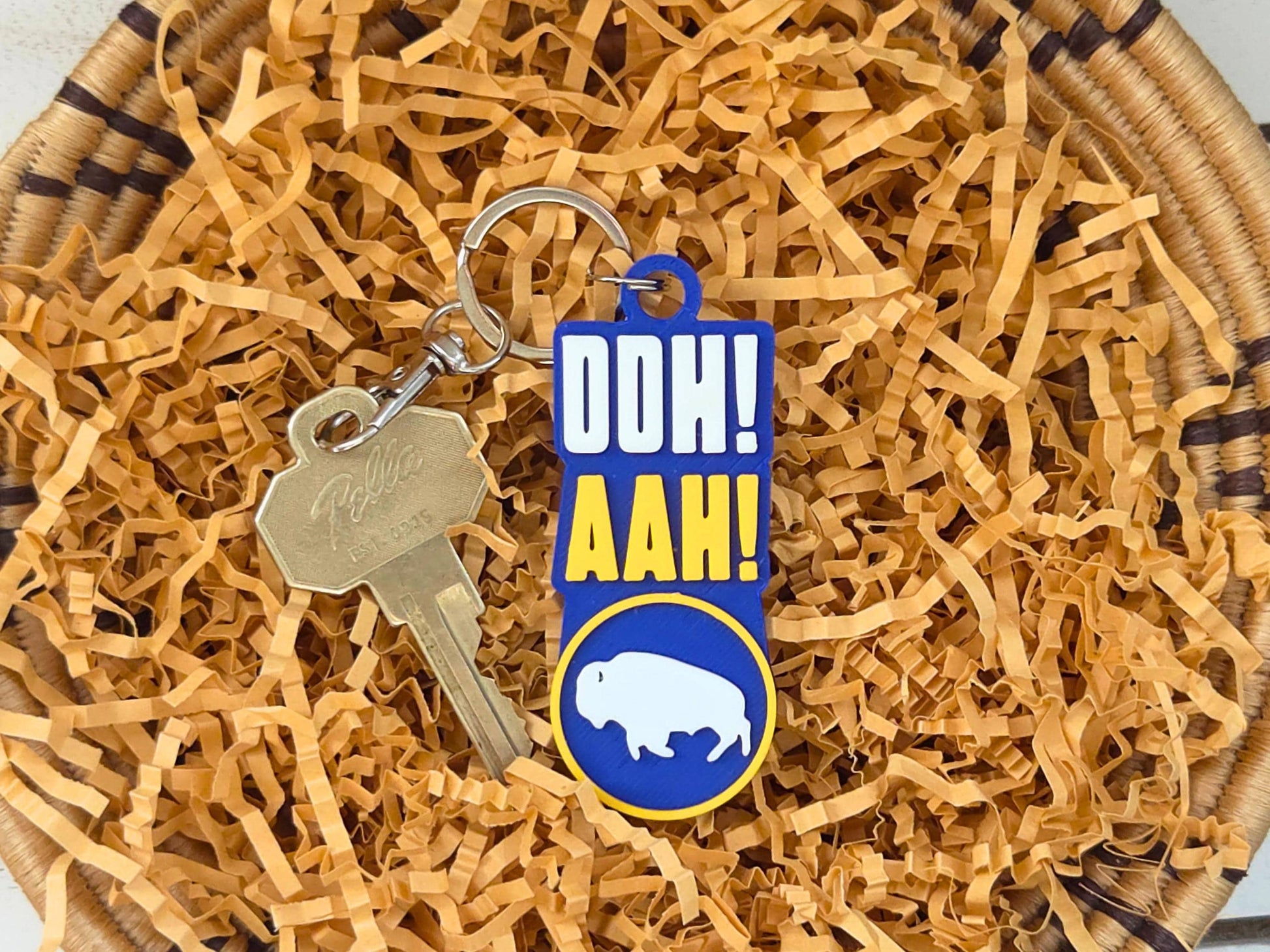 Blue and gold Buffalo fan keychain resting on tan gift basket filler, perfect for Mother's Day or game day gifts.