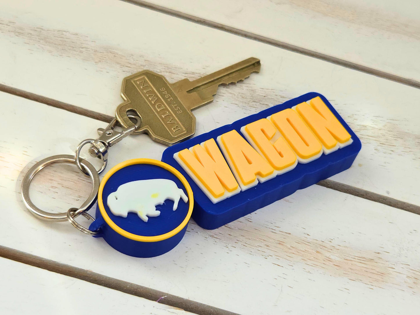 Buffalo "Wagon" hockey bag tag with lobster claw clip and house key on a white wood surface to show size and scale.